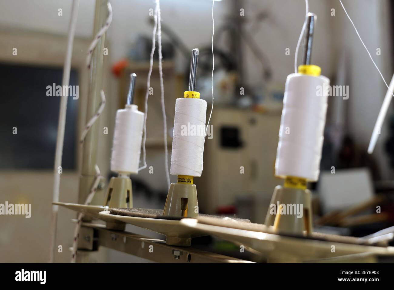 Les bobines de fil blanc sont debout sur un support à fils multiples, prêt à être utilisé sur une machine à coudre industrielle, représentant la précision dans les artisans textiles Banque D'Images