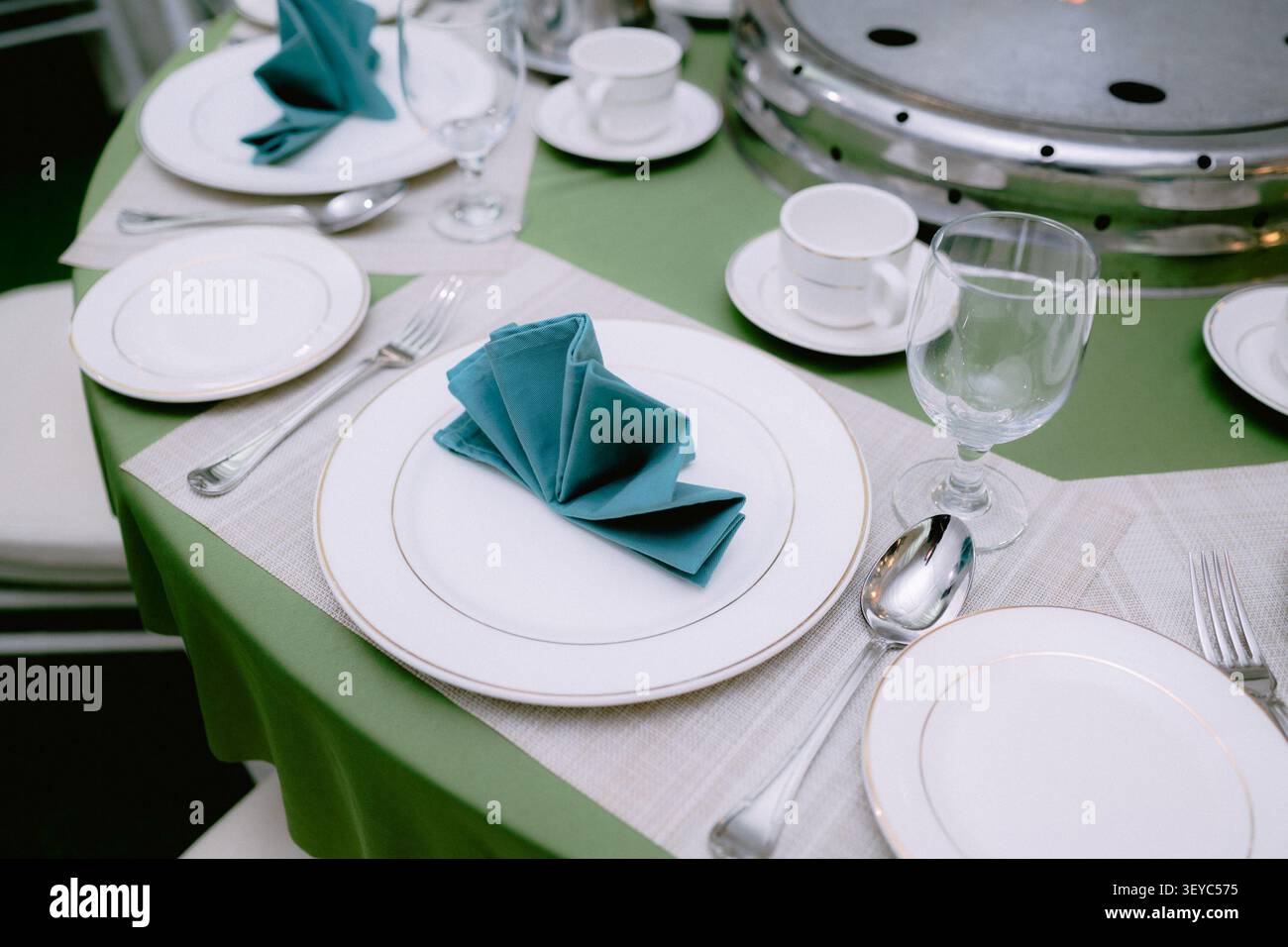 Élégante mise en table pour une réception de mariage avec des assiettes blanches, une serviette verte pliée, des couverts et de la vaisselle en verre. Banque D'Images