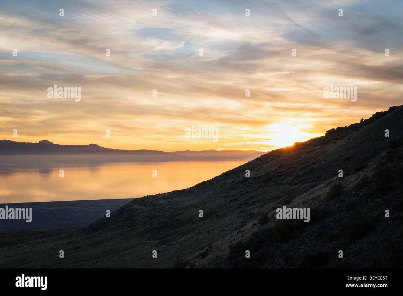 Paysage de coucher de soleil heure d'or à Antelope Island, Utah. Le soleil se couche derrière une pente de montagne sombre, projetant une lueur sur le Grand Lac Salé. Banque D'Images