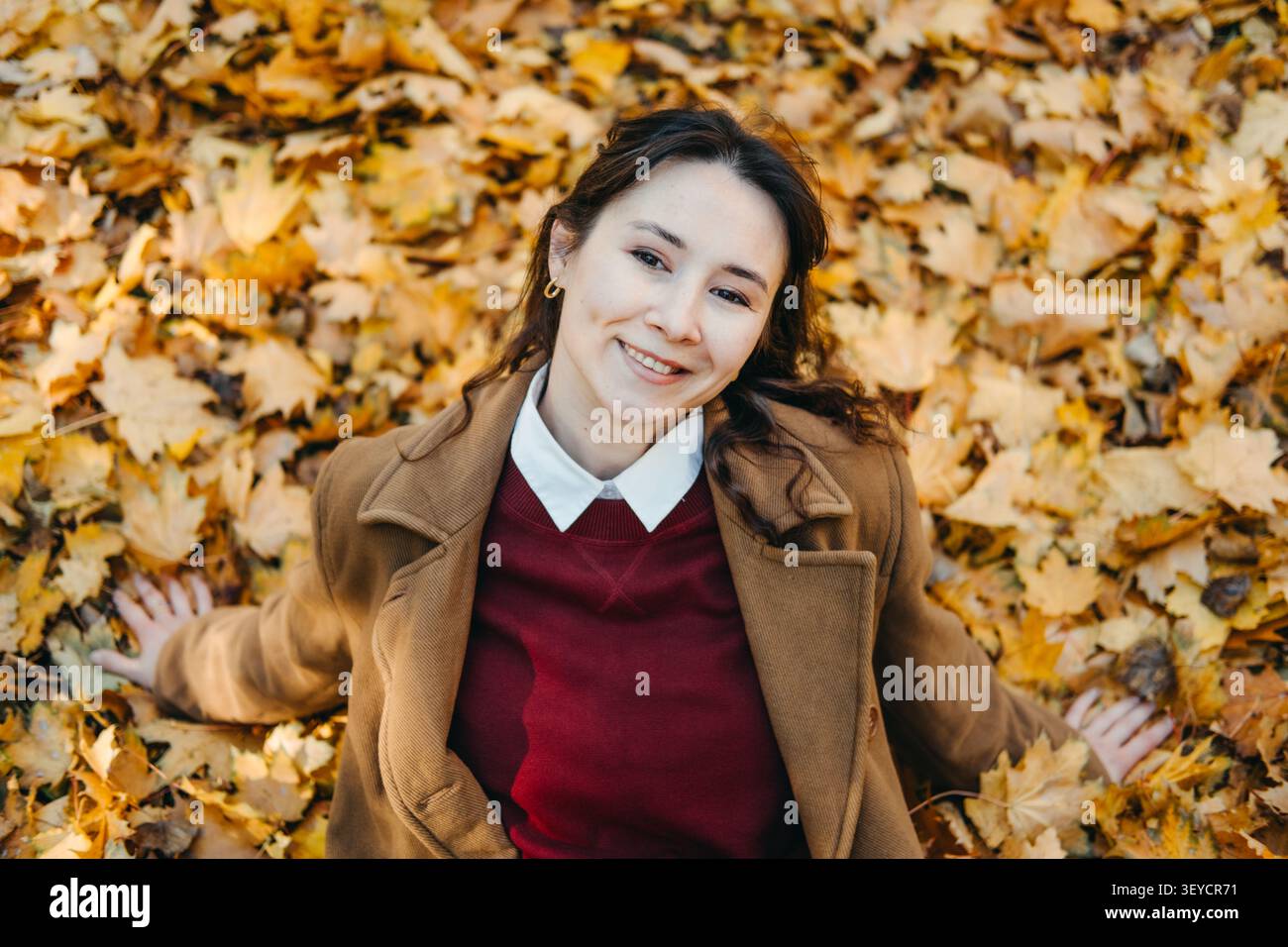 Femme souriante se trouve sur le sol couvert de feuilles d'automne regardant vers le haut. Détox numérique employé de bureau, concept de congé personnel, gestion du stress pour Banque D'Images
