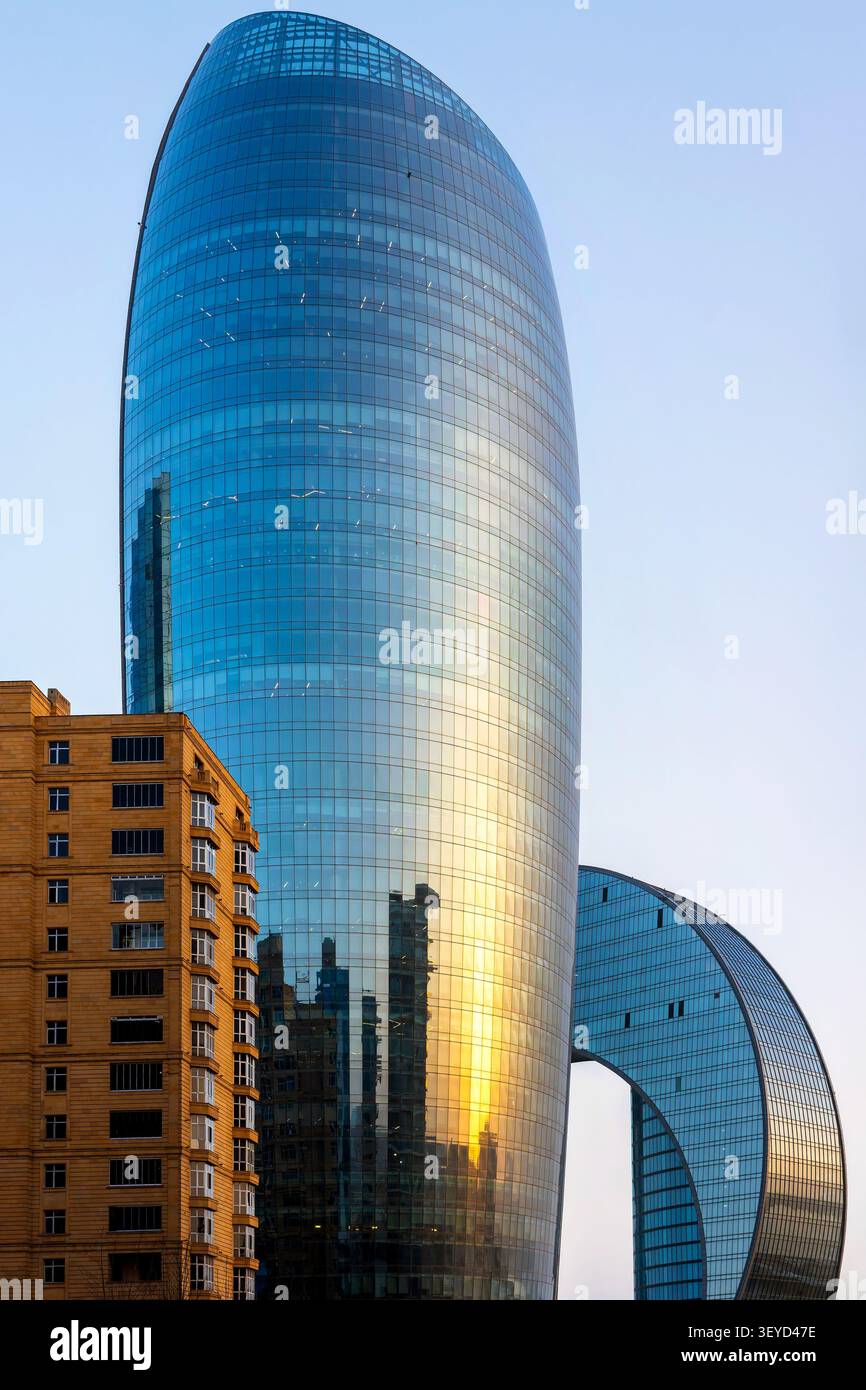 Façade en verre incurvée de Port Baku Tower 2 reflétant la lumière dorée du coucher du soleil avec l'arc de l'hôtel Crescent visible sur la droite. Bakou, Azerbaïdjan. Banque D'Images