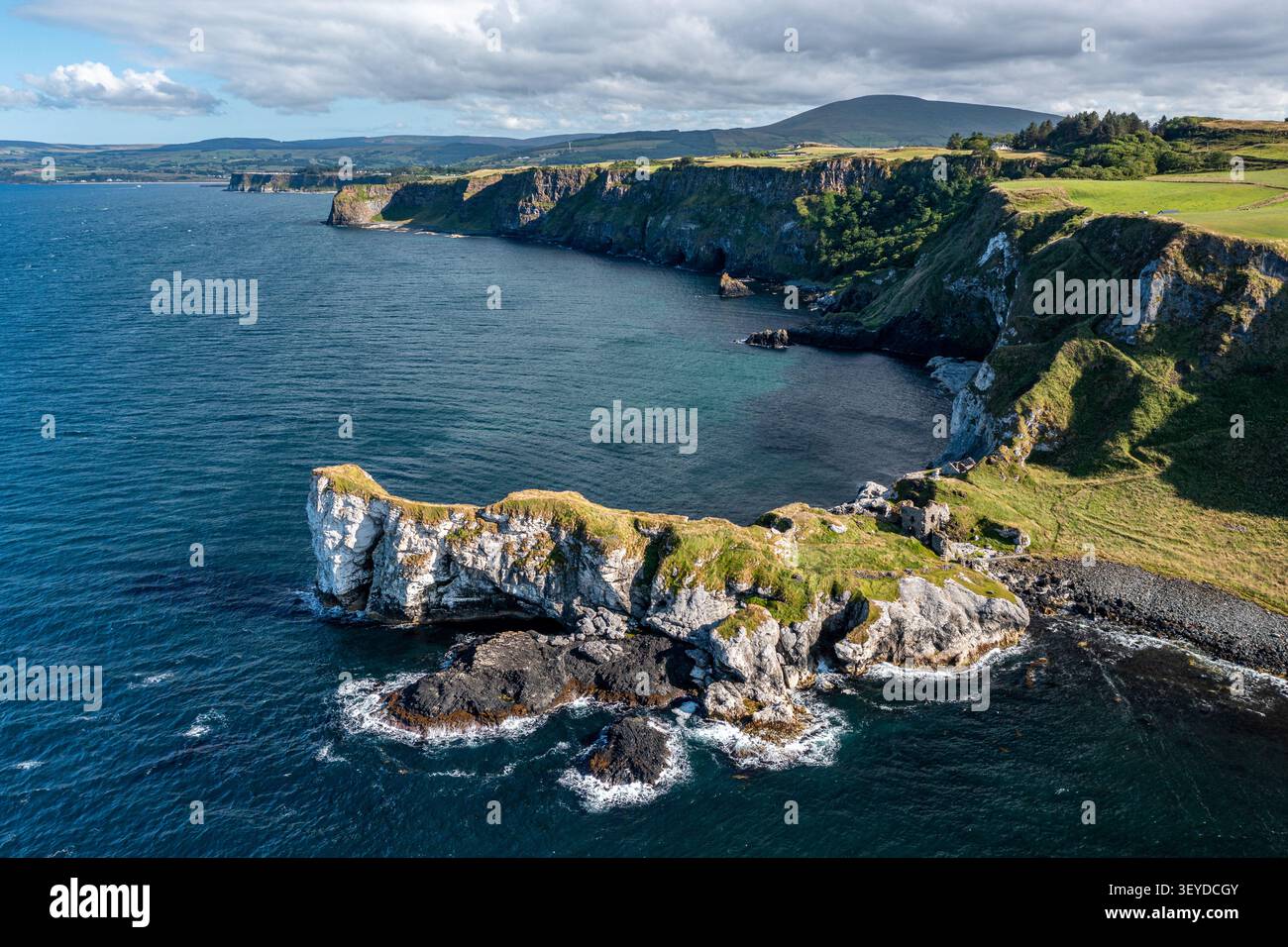 Paysage aérien de falaises côtières escarpées et de promontoires herbeux rencontrant la mer bleue profonde. Les nuages spectaculaires, le littoral rocheux et la baie calme évoquent la côte Banque D'Images