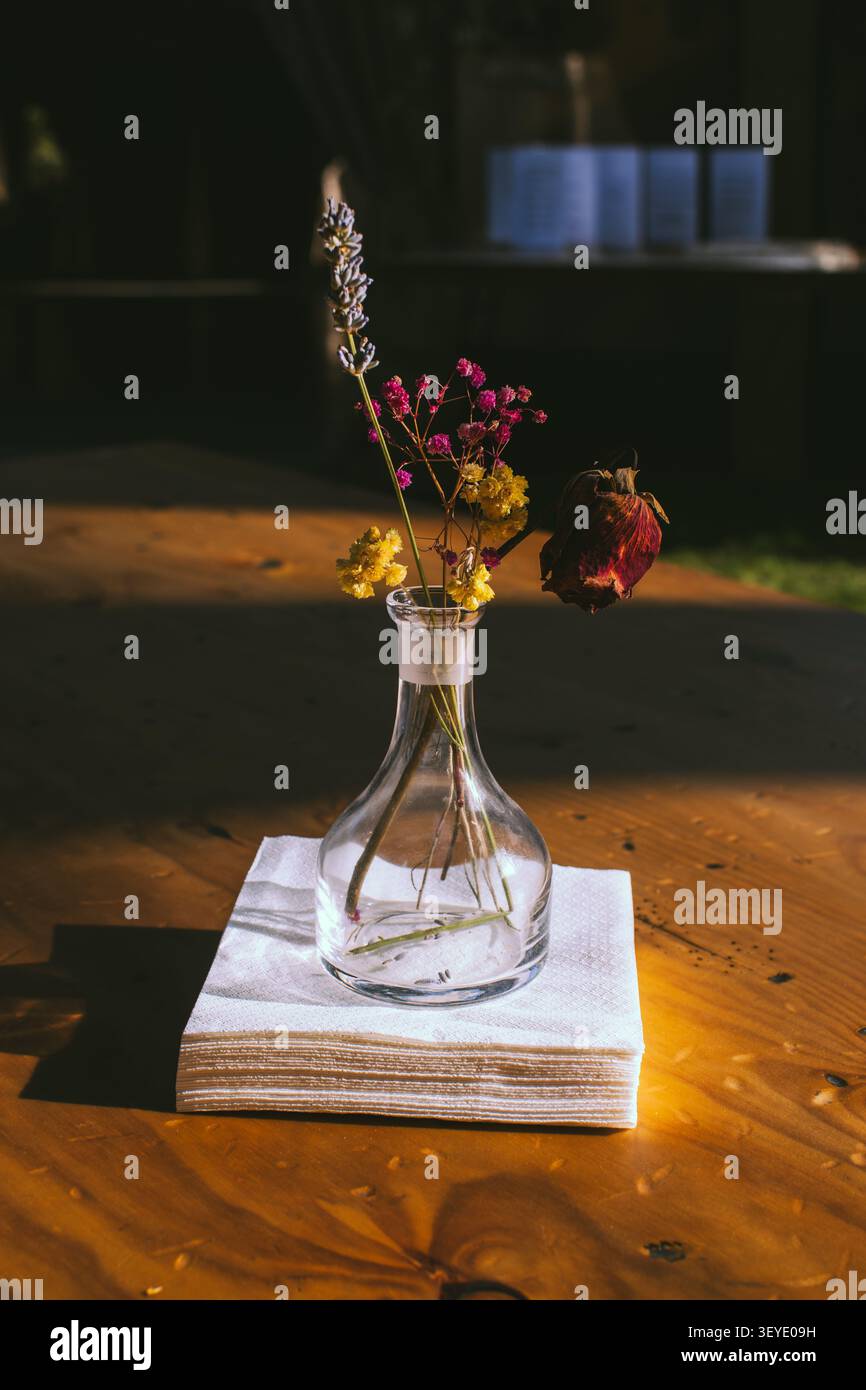 Arrangement de fleurs séchées dans un vase en verre transparent sur une serviette blanche pliée sur une table en bois baignée de lumière naturelle Banque D'Images
