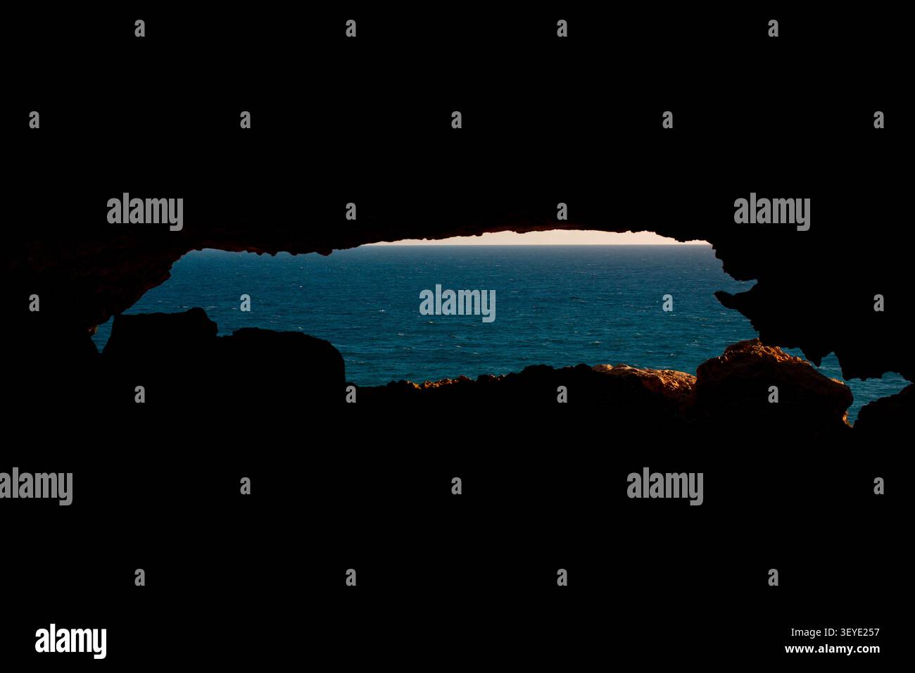 Vue sur la mer Méditerranée à travers l'ouverture d'une grotte côtière, avec des silhouettes de roches sombres encadrant l'eau bleue. Banque D'Images