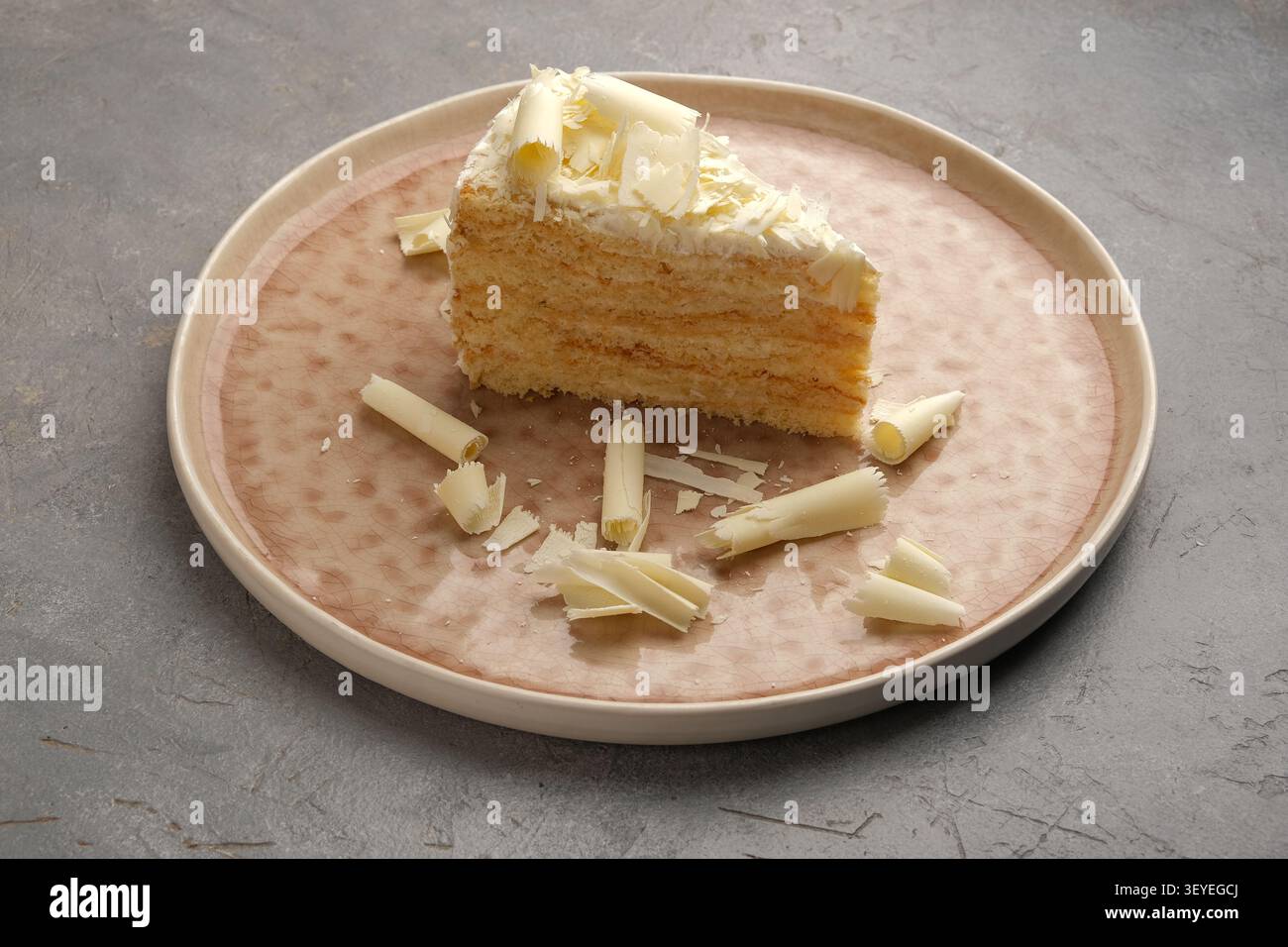 Tranche de gâteau en couches avec des boucles de chocolat blanc sur une plaque en céramique sur fond gris Banque D'Images