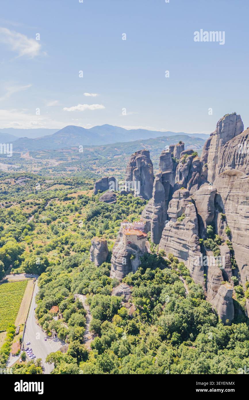 Prise de vue aérienne verticale par drone d'un ancien monastère orthodoxe debout sur un pic de falaise abrupte au-dessus d'une route asphaltée sinueuse avec des voitures garées dans un vert fo Banque D'Images