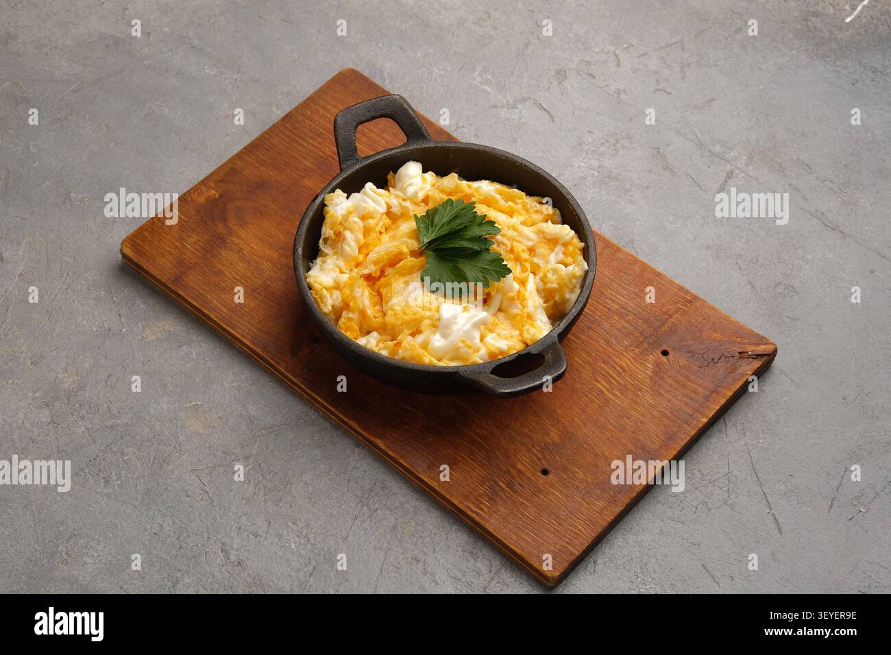 Oeufs brouillés rustiques dans une poêle en fonte sur planche de bois sur fond de pierre grise Banque D'Images