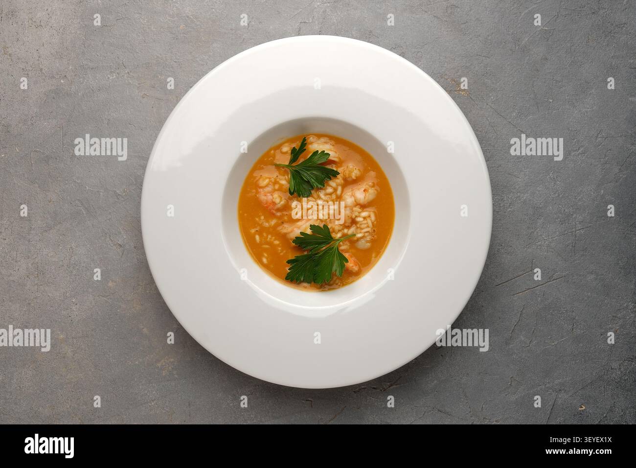Assiette blanche avec risotto aux crevettes servie en sauce orange sur table en pierre grise Banque D'Images