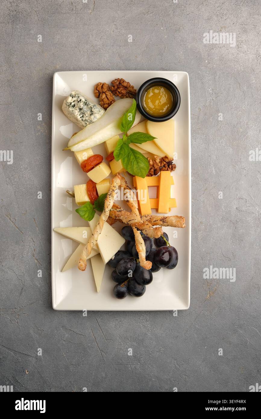Plateau de fromage élégant avec raisins poire noix basilic et gressins sur la surface de pierre Banque D'Images