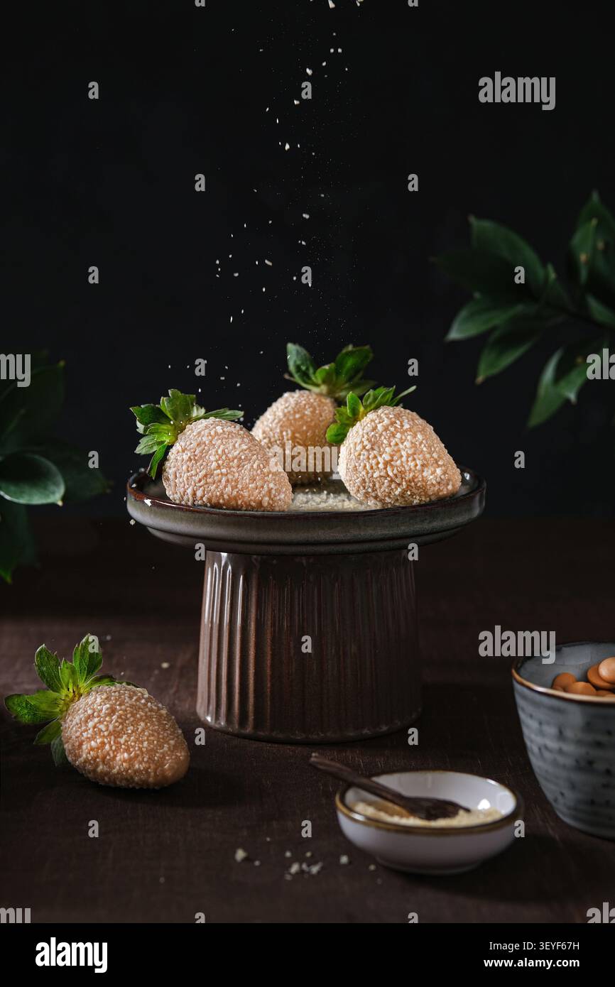 Boules de dessert enrobées de sésame sur un piédestal en céramique avec fond sombre et feuilles Banque D'Images