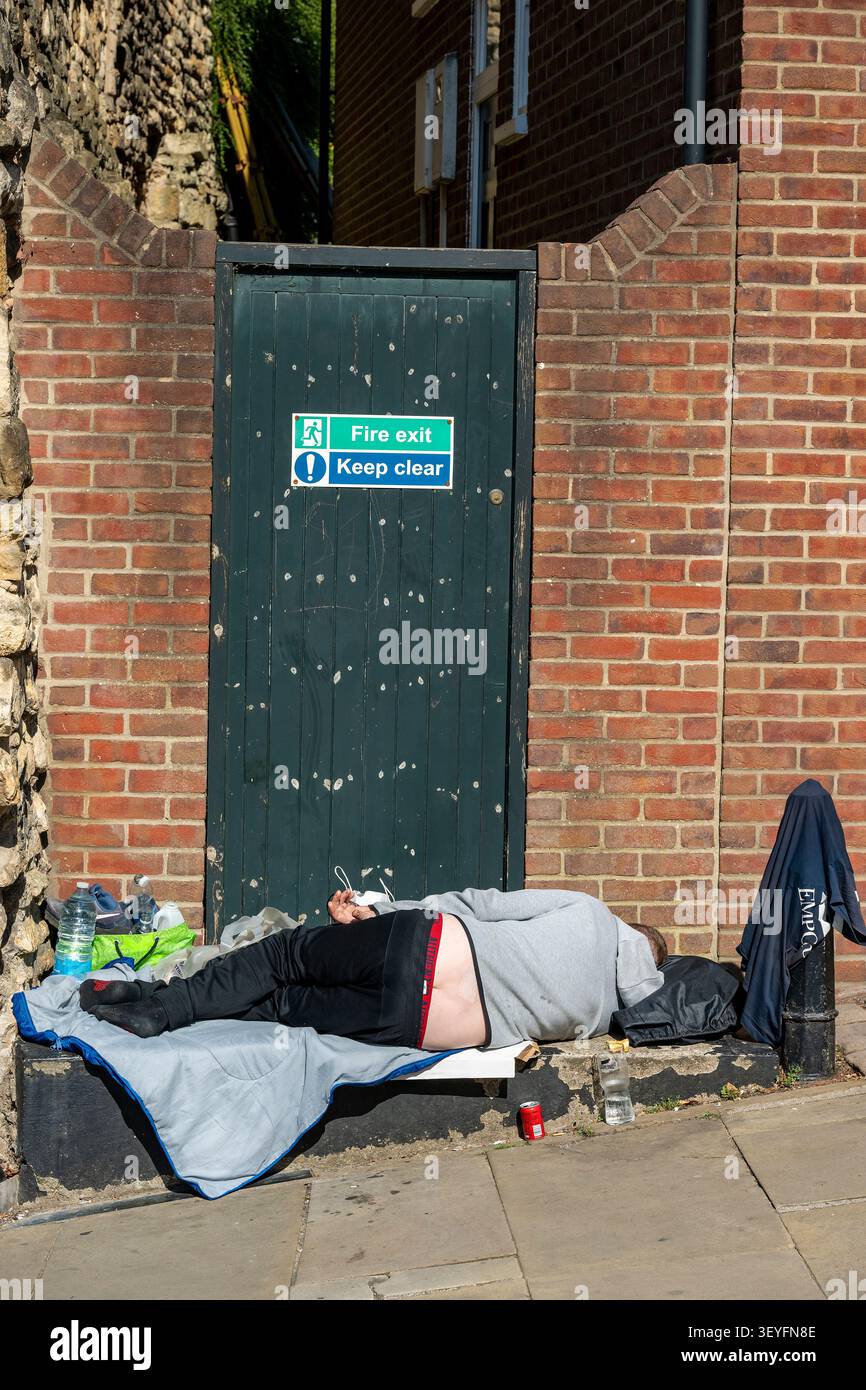 Personne sans-abri endormie sur une marche devant une porte dans le centre-ville de Lincoln, Lincolnshire, Angleterre, Royaume-Uni Banque D'Images