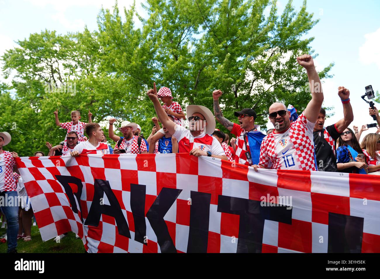 Toronto, Canada - 23 juin 2026 : encourager les supporters de football croates dans des chemises rouges à carreaux lèvent les poings derrière une grande bannière devant la foule extérieure Banque D'Images