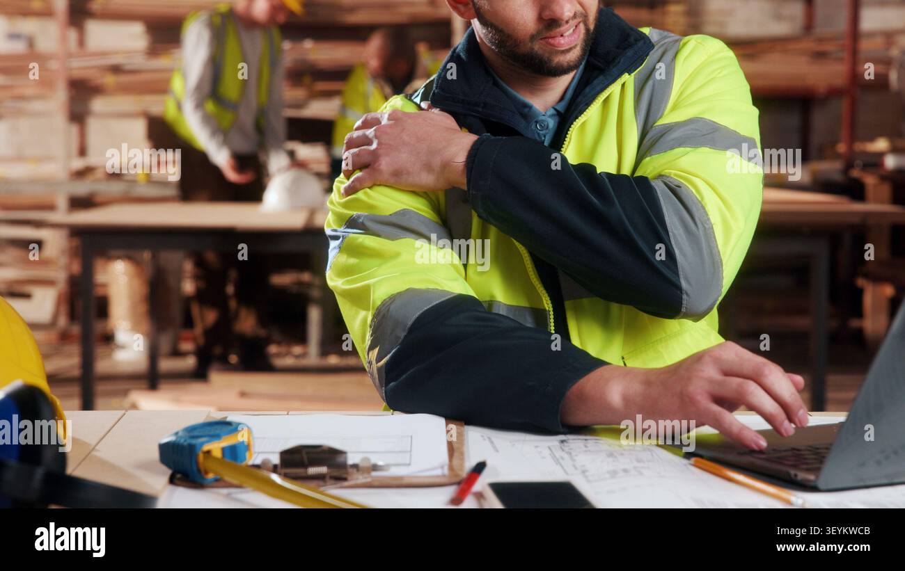 Menuisier, mains et douleurs à l'épaule en atelier avec ordinateur portable, fatigue ou épuisement professionnel dans l'industrie. Planification de projet, tech ou homme dans l'usine de travail du bois avec Banque D'Images