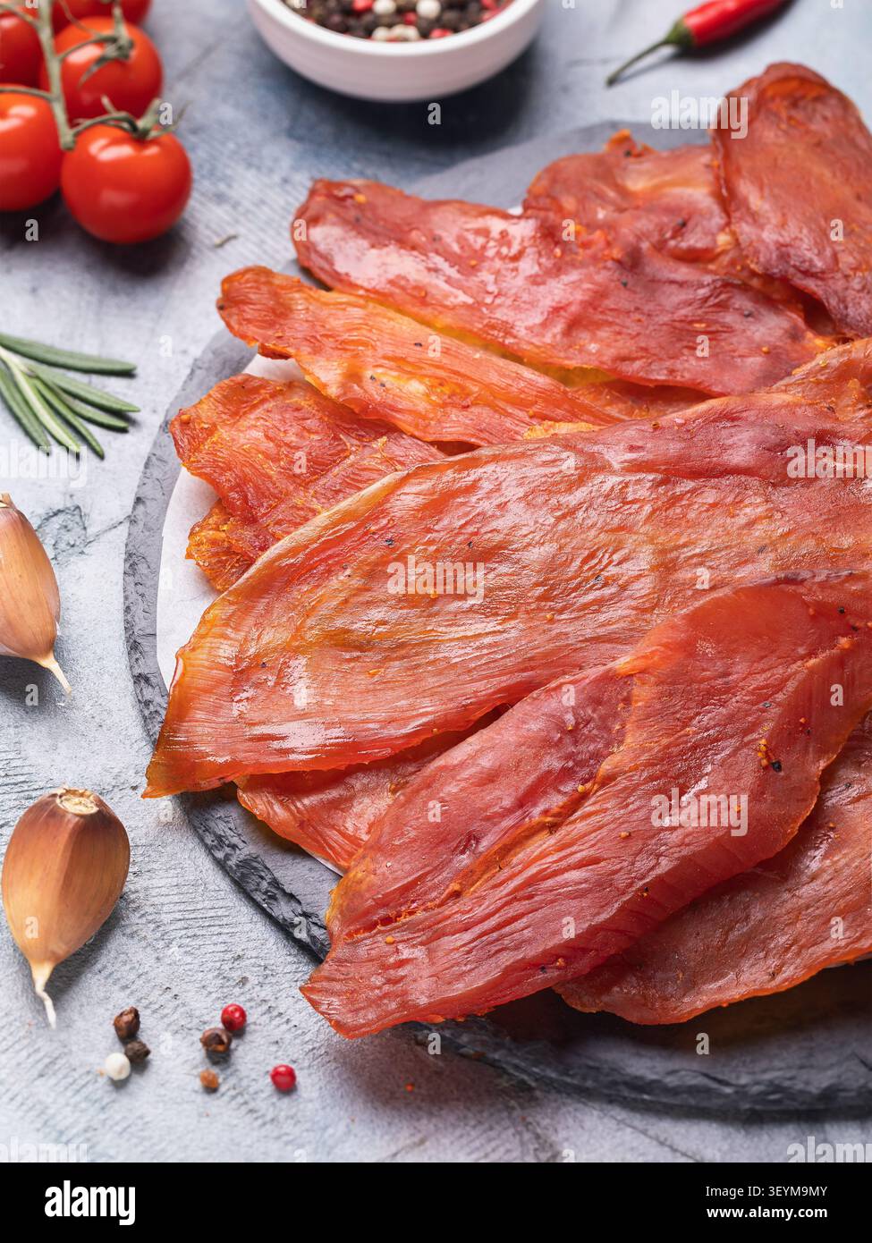 Filet de dinde séchée fumé épicé avec assaisonnements sur planche d'ardoise avec tomates cerises, ail et poivre Banque D'Images