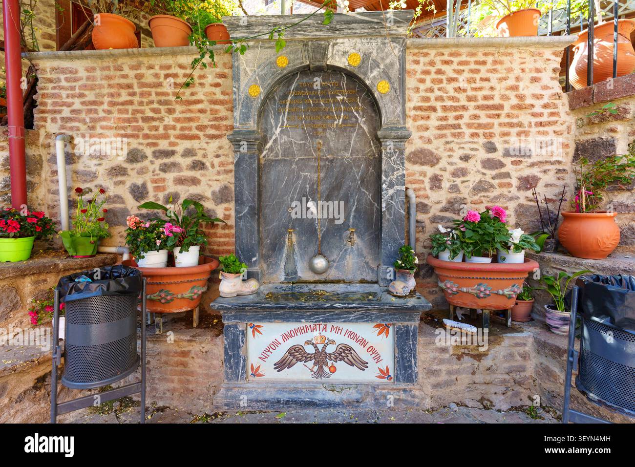 Lesbos, Grèce - 23 avril 2026 : fontaine d'eau potable historique en marbre décorée d'un relief d'aigle à double tête, flanquée de pots de fleurs à Taxi Banque D'Images