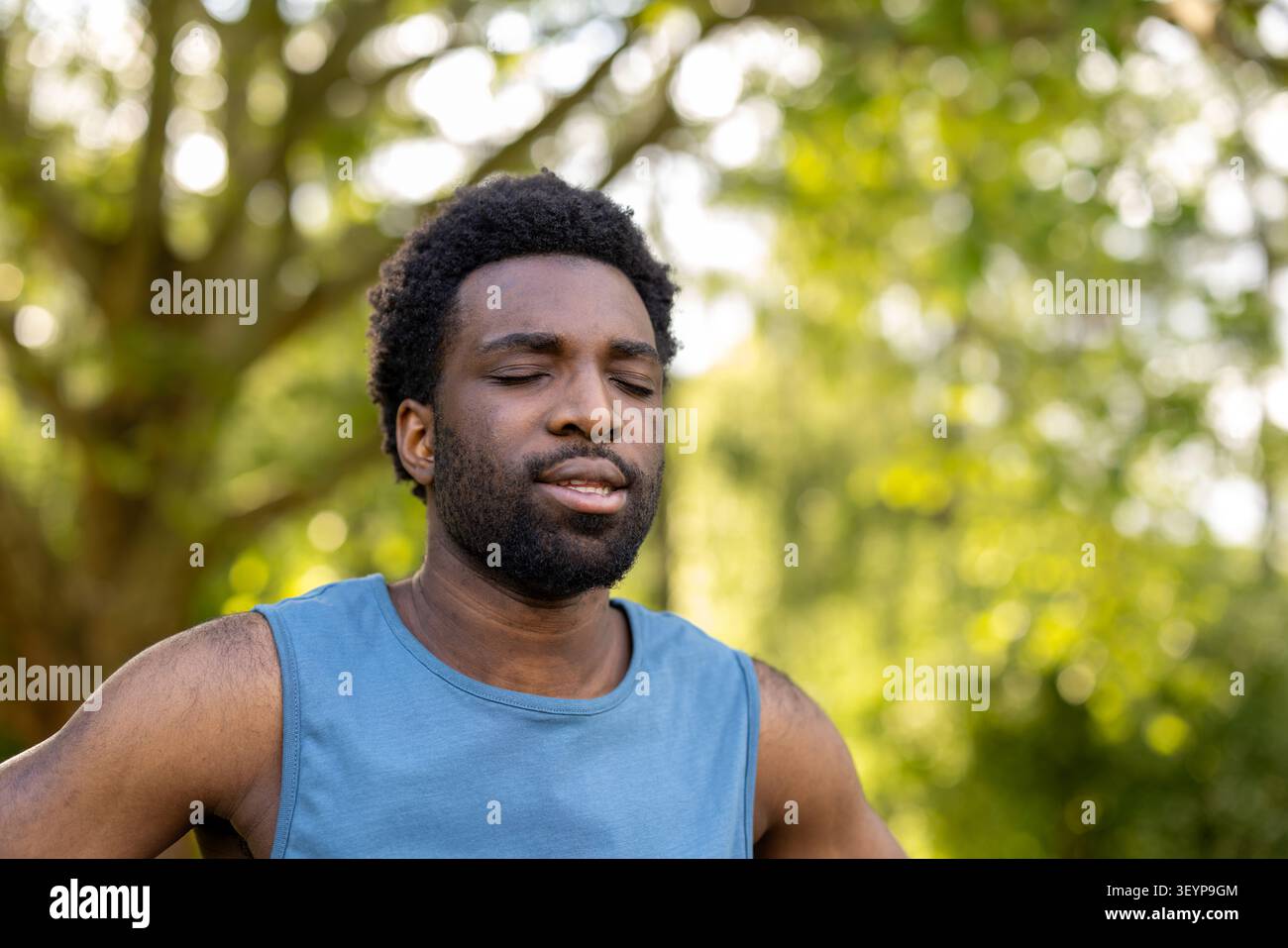 Jeune homme debout dehors, les yeux fermés, trouvant la pleine conscience et la paix intérieure dans la nature, pratiquant des activités de relaxation et de bien-être Banque D'Images