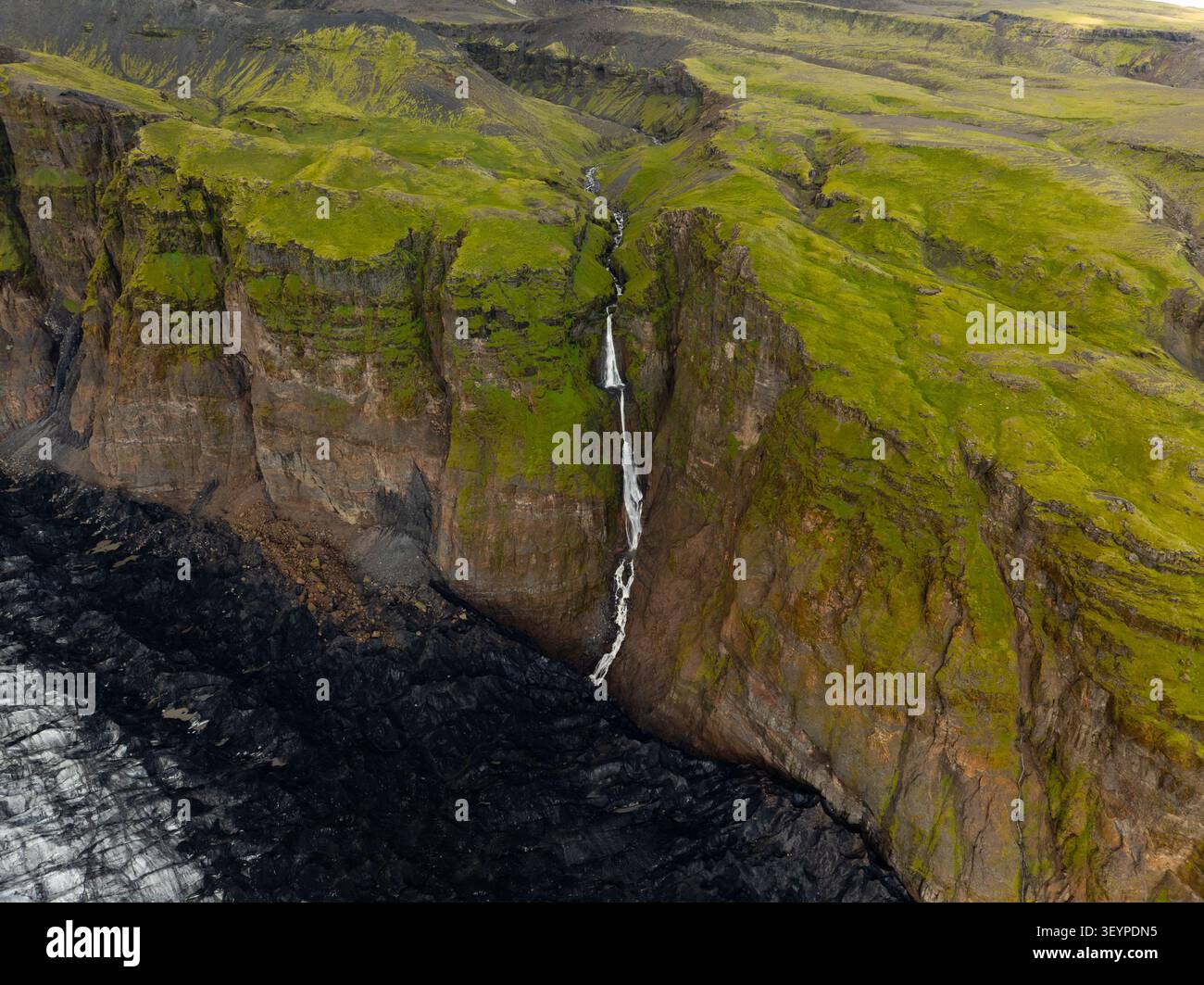 Vue aérienne du glacier Solheimajokull avec une cascade descendant les falaises volcaniques abruptes couvertes de mousse à Myrdalshreppur, en Islande. Banque D'Images