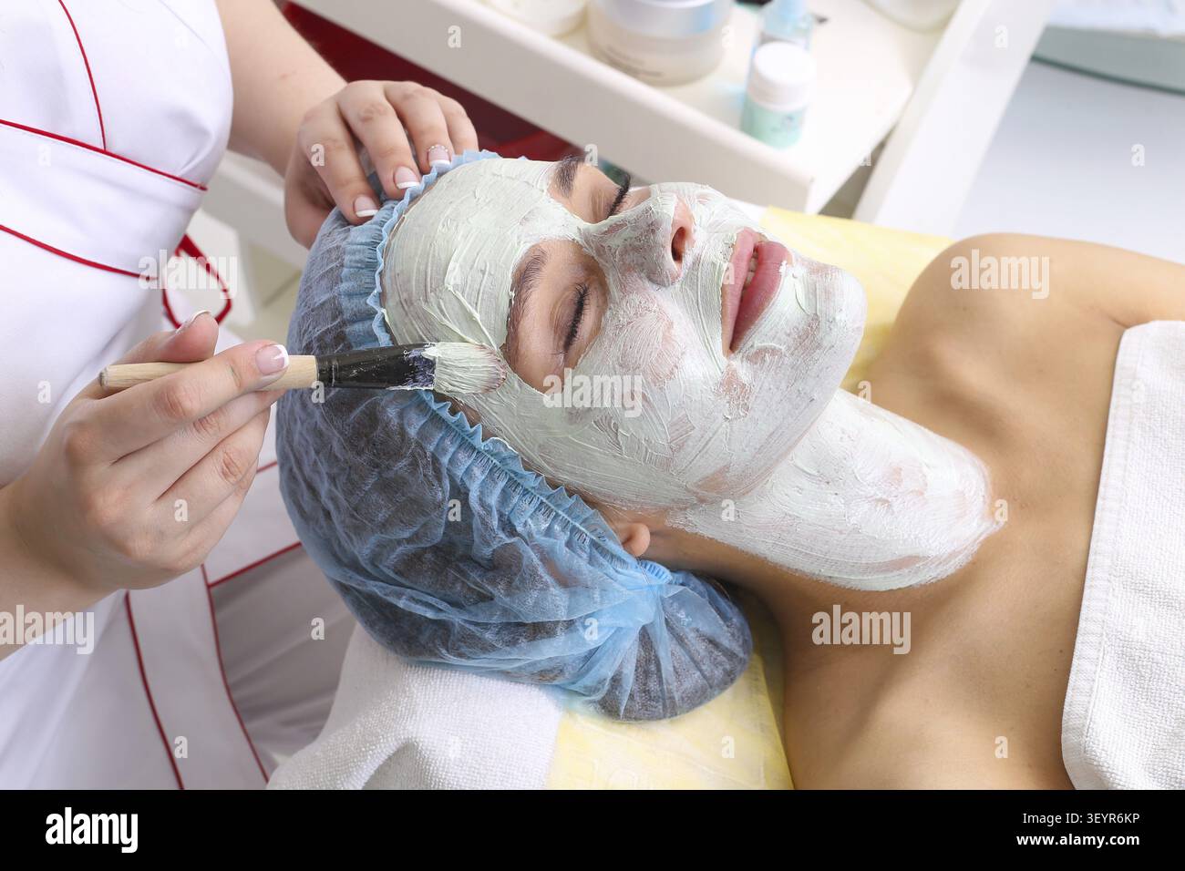 Cosmetician appliquant le masque facial à la face de belle jeune femme dans spa salon Banque D'Images