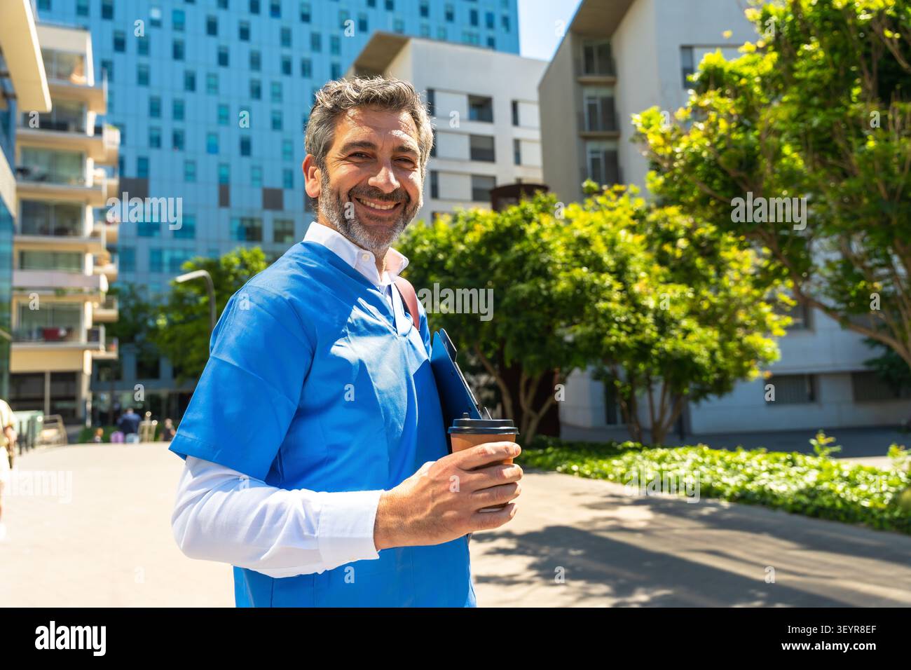 Docteur souriant dans des gommages tenant du café devant l'hôpital Banque D'Images