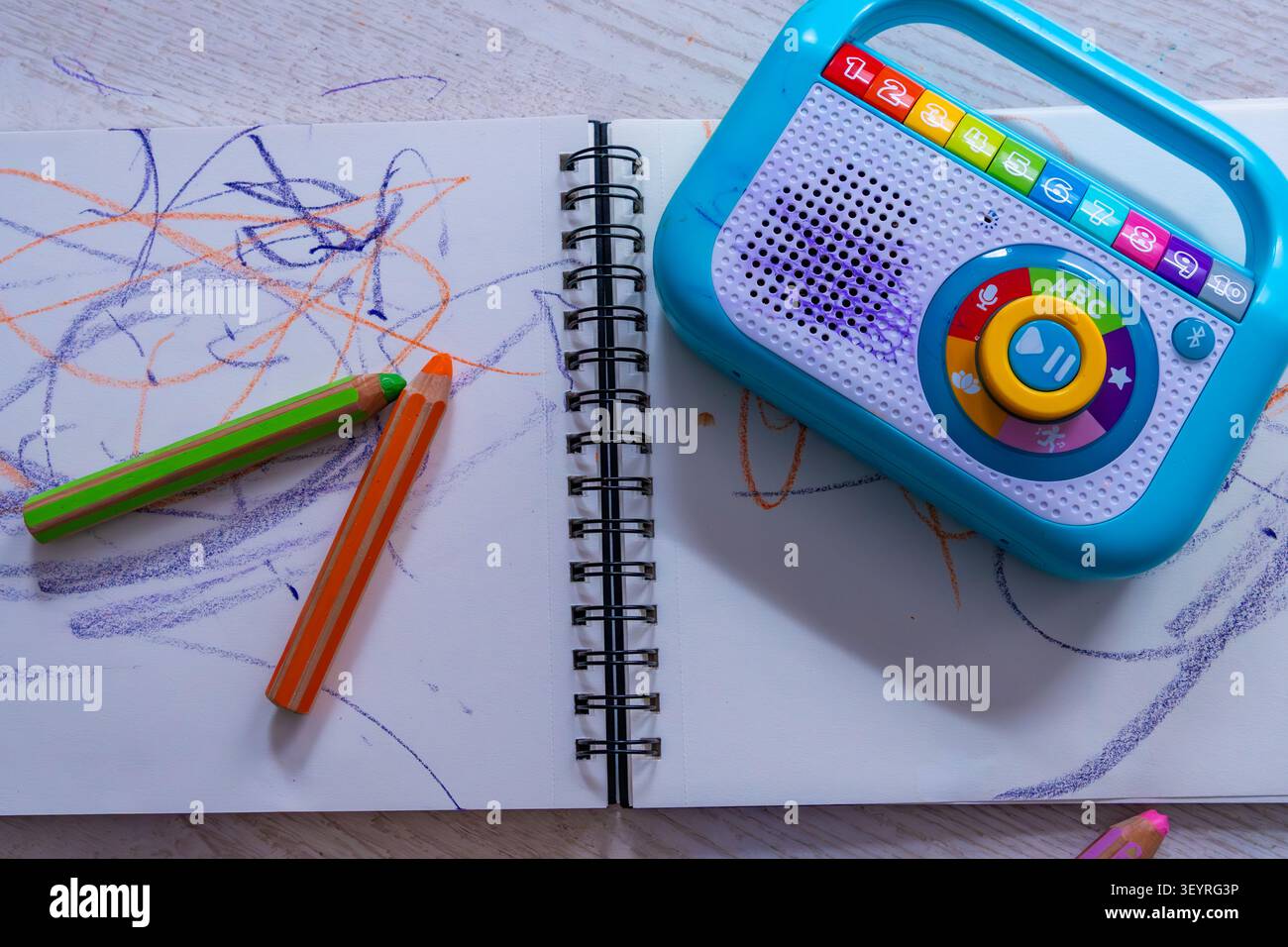 Vue de dessus d'un carnet de croquis avec des gribouilles colorées pour enfants, des crayons de couleur épais et un lecteur de musique de jouet éducatif. L'activité créative m'encourage Banque D'Images