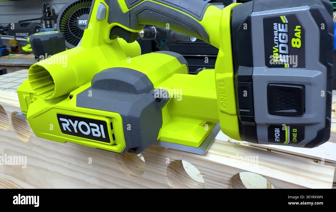 Une raboteuse électrique sans fil vert citron et gris repose sur une planche de bois avec des trous de perçage. Banque D'Images
