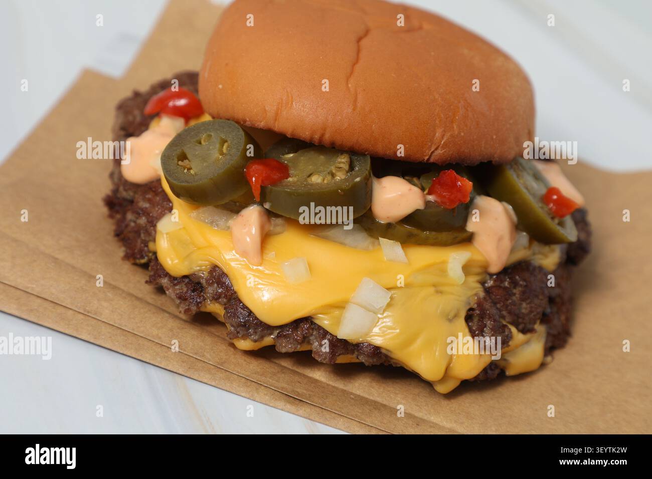 Un hamburger est posé sur un support en papier. Le pain est sur le dessus. La viande est dessous, avec du fromage fondant. Il y a a des jalapeños et de Banque D'Images