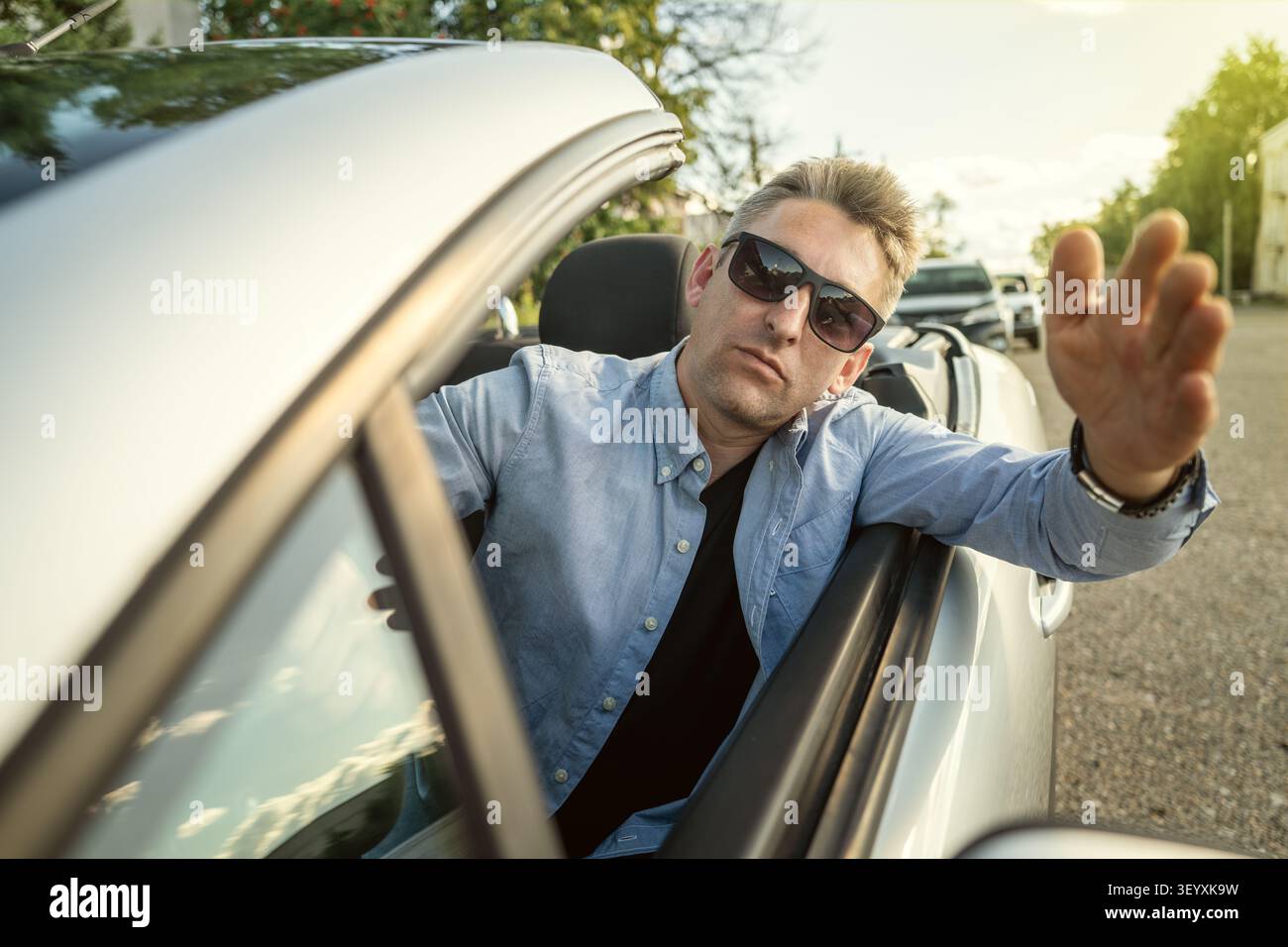 Homme d'affaires en colère gesticulant de manière agressive et criant alors qu'il est coincé dans les embouteillages. Crise de colère au volant, retard et stress de la conduite urbaine. Banque D'Images