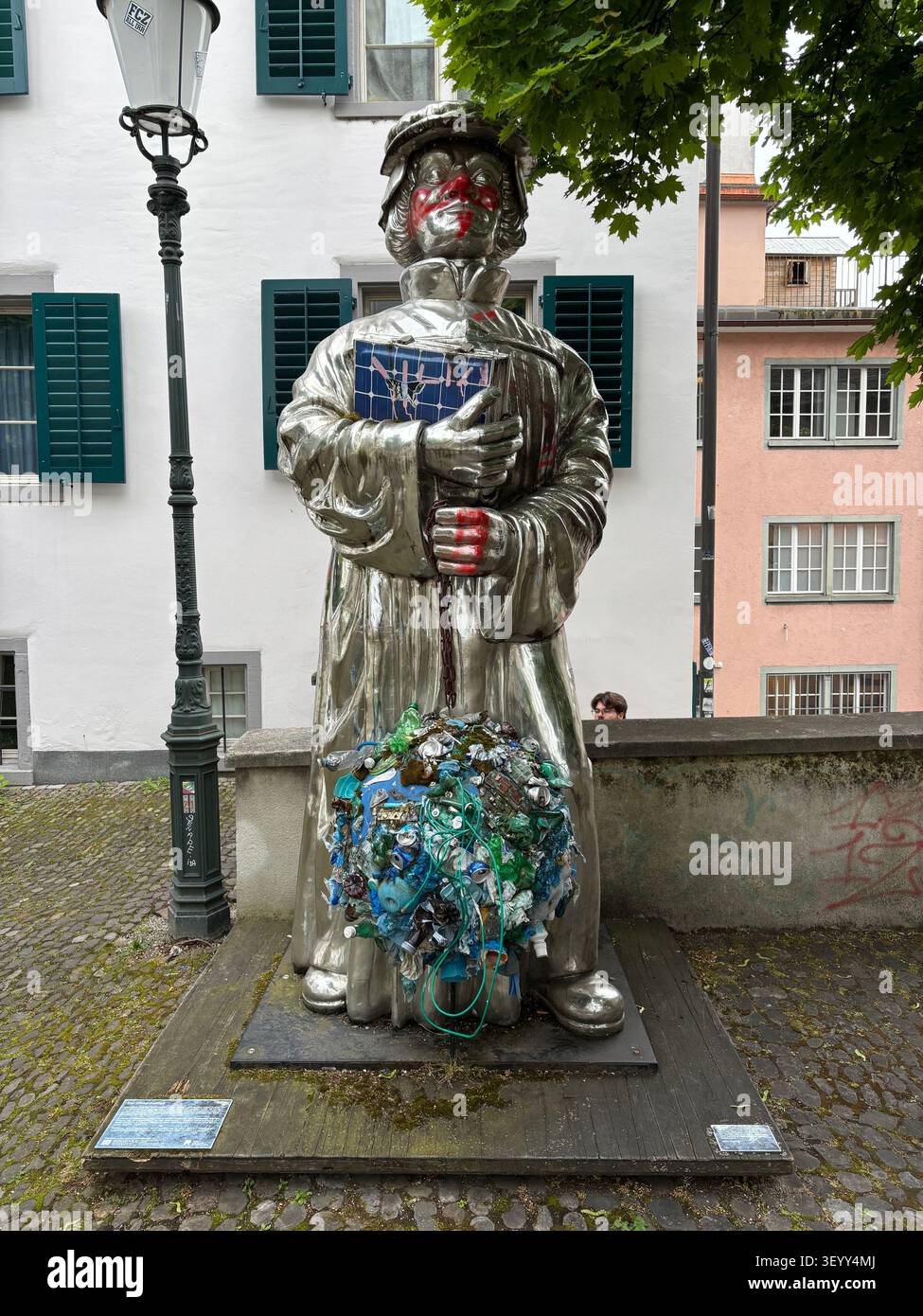 Une statue en métal poli controversée d'un réformateur religieux couverte de graffitis modernes et d'art de déchets plastiques à Zurich - Image de stock capturée avec un smartphone