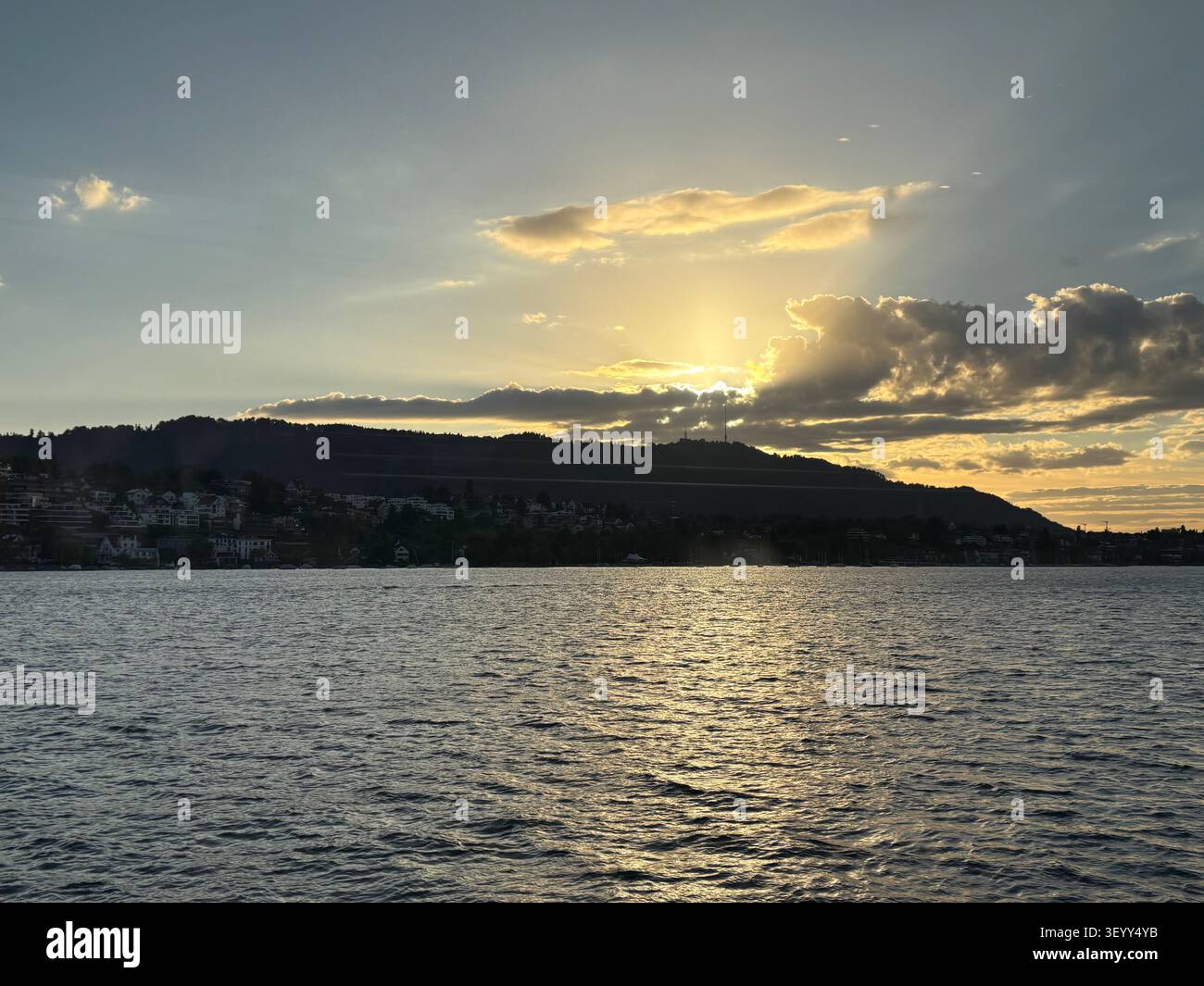 Le soleil se couchant derrière les collines du lac de Zurich, projetant une lueur dorée sur les ondulations de l'eau, Zurich, Suisse - Image de stock capturée avec un smartphone