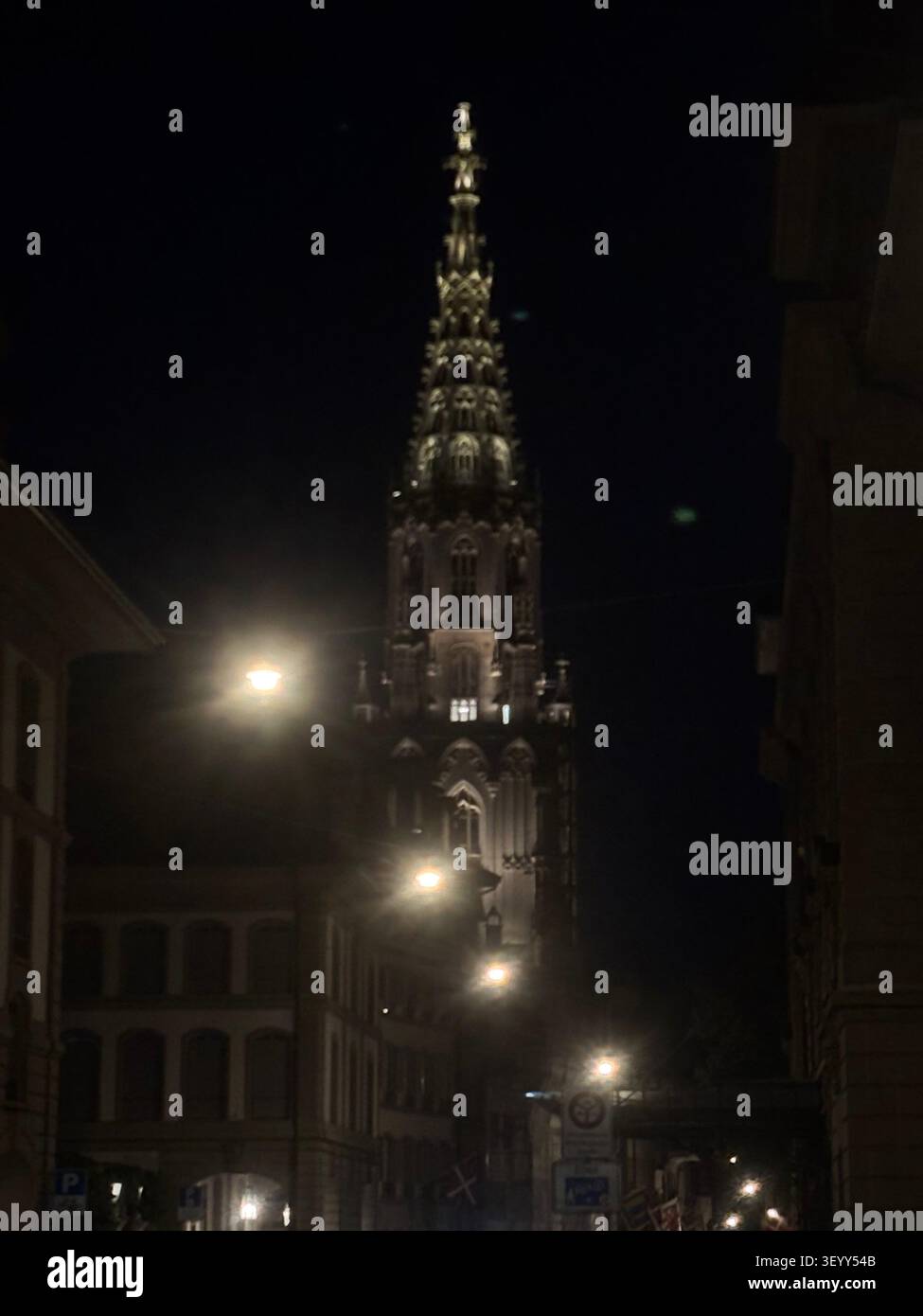Vue nocturne de la flèche gothique illuminée de la cathédrale de Berne (Berner Minster) encadrée par des lampadaires à Berne, Suisse Banque D'Images