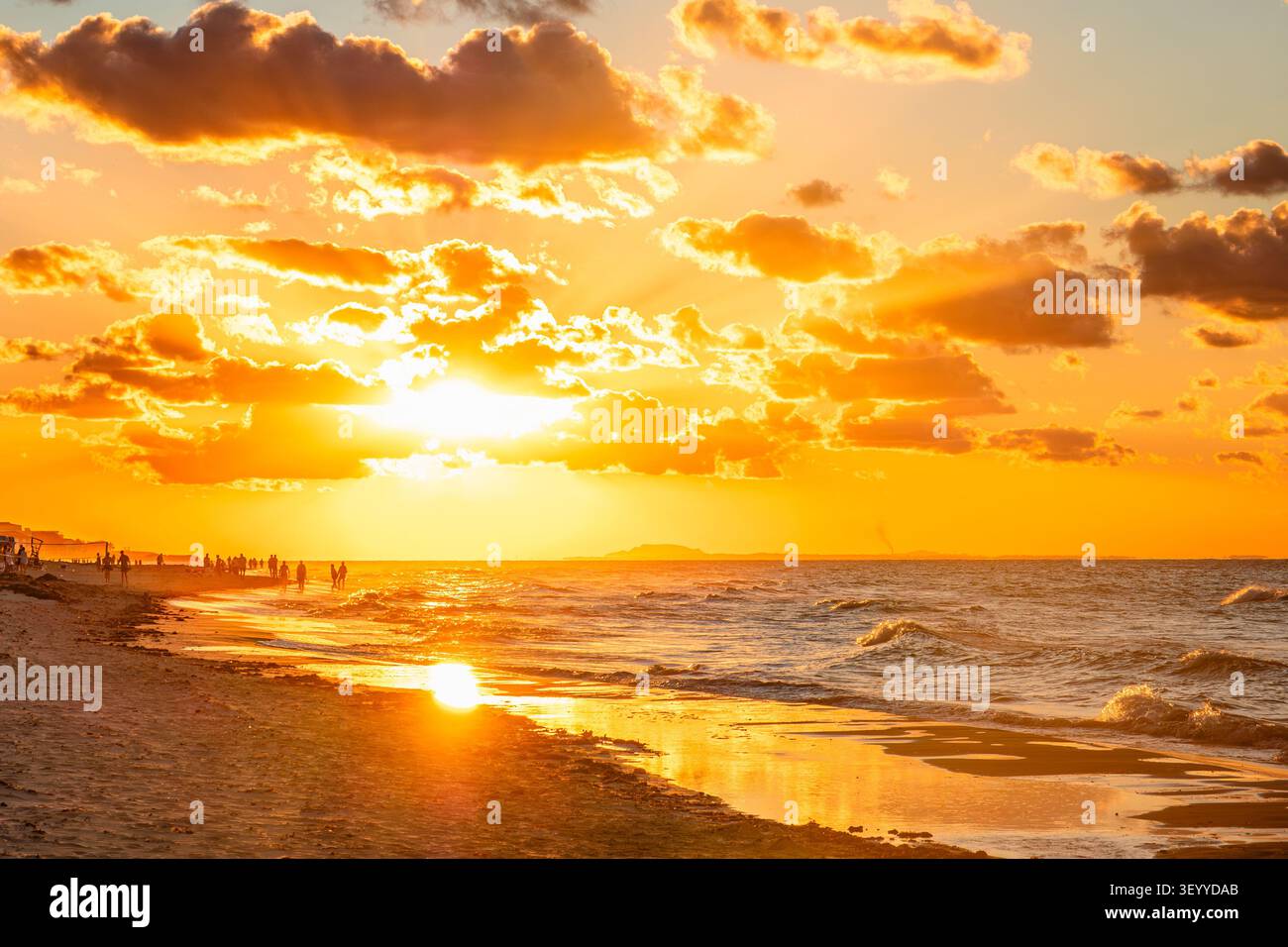 Beau coucher de soleil sur la plage avec des gens animés profitant de la promenade du soir au bord de la mer. Banque D'Images