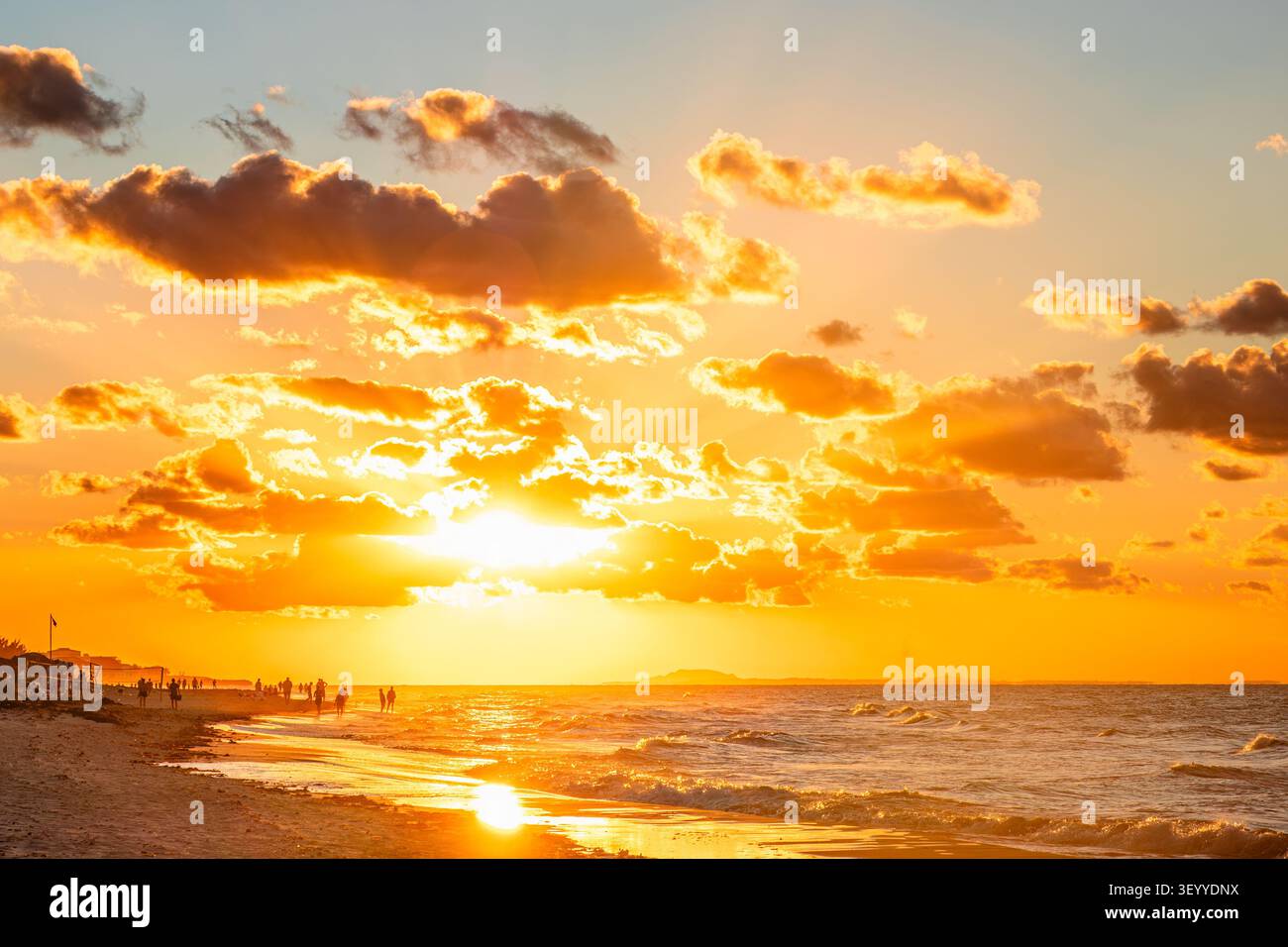 Beau coucher de soleil sur la plage avec des gens animés profitant de la promenade du soir au bord de la mer. Banque D'Images