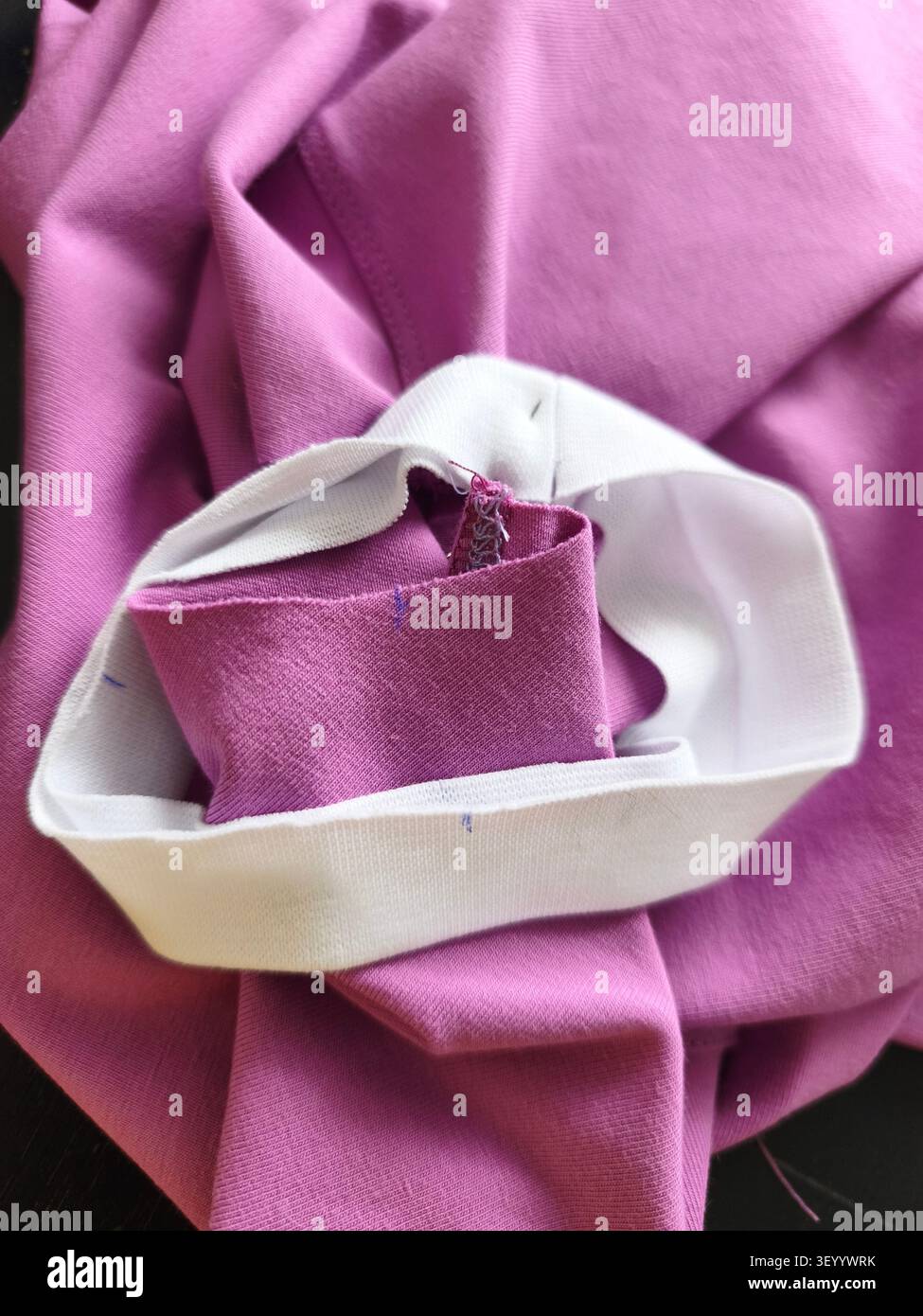 Le travailleur de couture épingle la garniture blanche au matériel de tricot violet avant de coudre sur la machine à coudre, les détails de production de vêtements. Industriel, Arts Banque D'Images