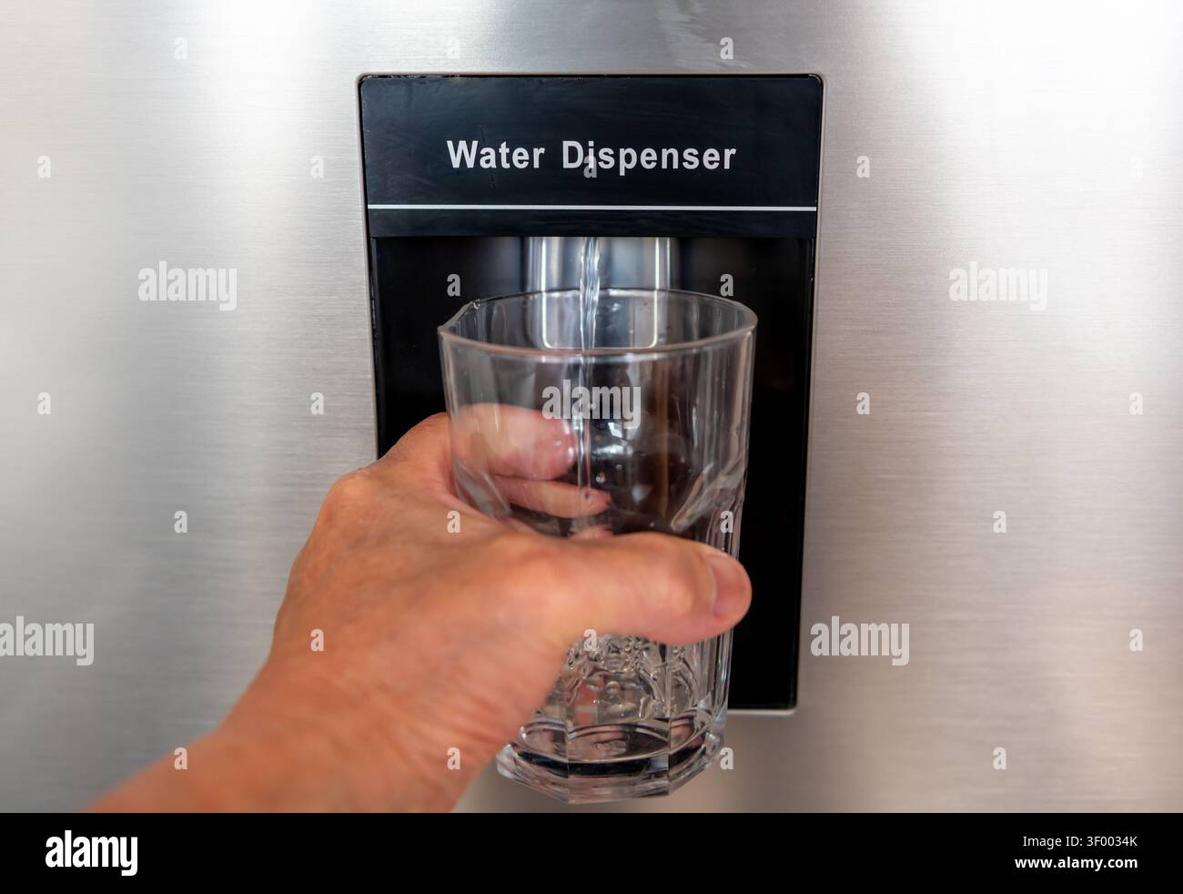 Gros plan d'une personne recevant un verre d'eau réfrigérée d'un distributeur d'eau de réfrigérateur. Banque D'Images