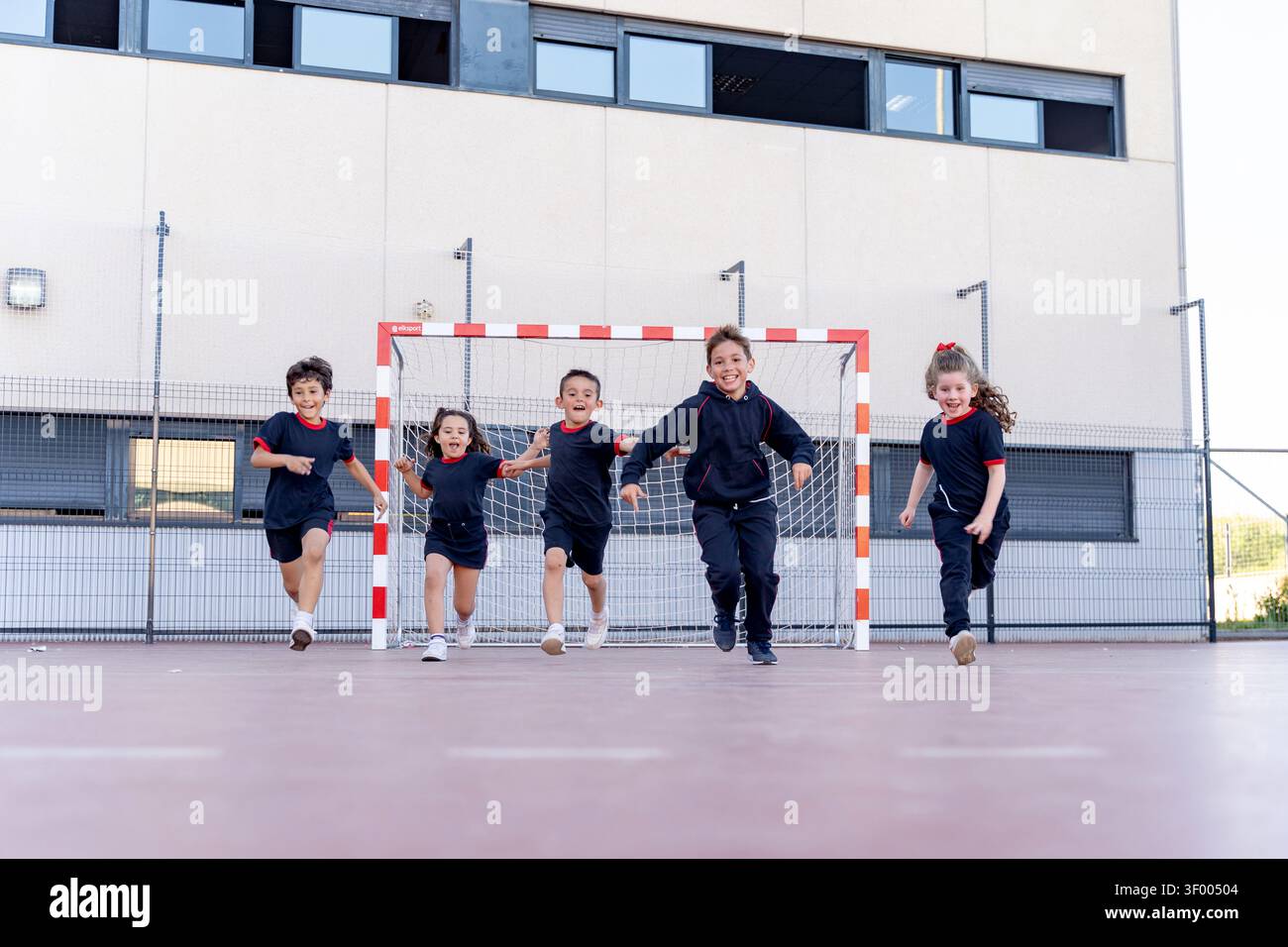Écoliers en uniforme courant et riant sur un terrain de sport extérieur, s'amusant pendant le cours d'éducation physique Banque D'Images