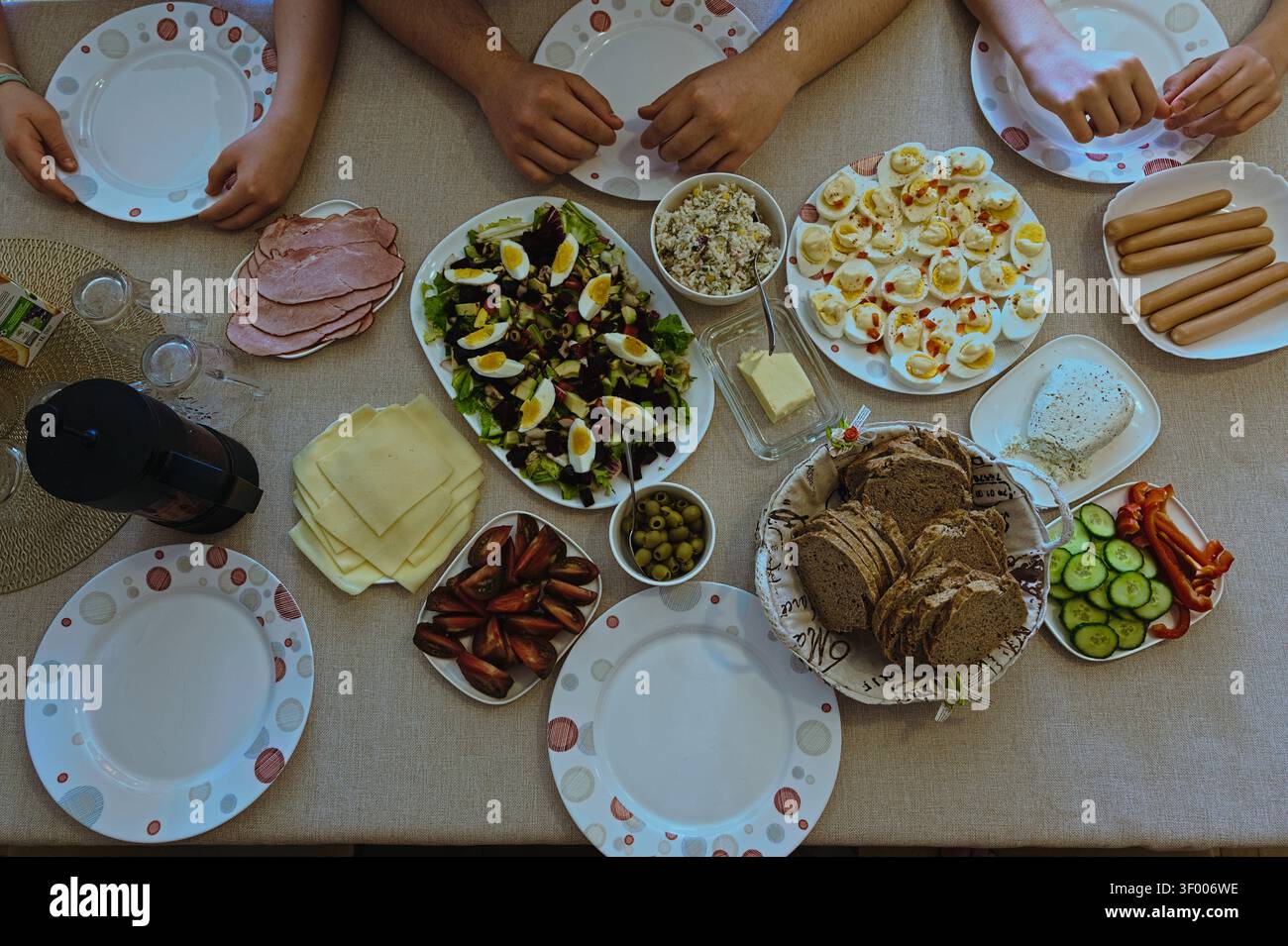 Repas de petit-déjeuner en famille sur une table avec du pain, des œufs, de la salade et des mains qui s'y plongent. Banque D'Images