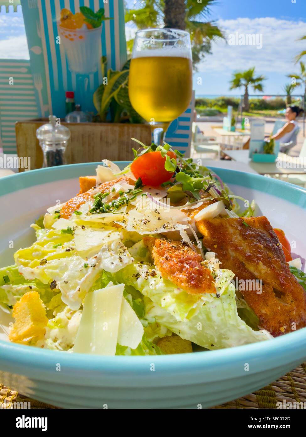 Salade César avec poulet grillé et fromage parmesan servi avec un verre de bière dans un restaurant extérieur en bord de mer Banque D'Images
