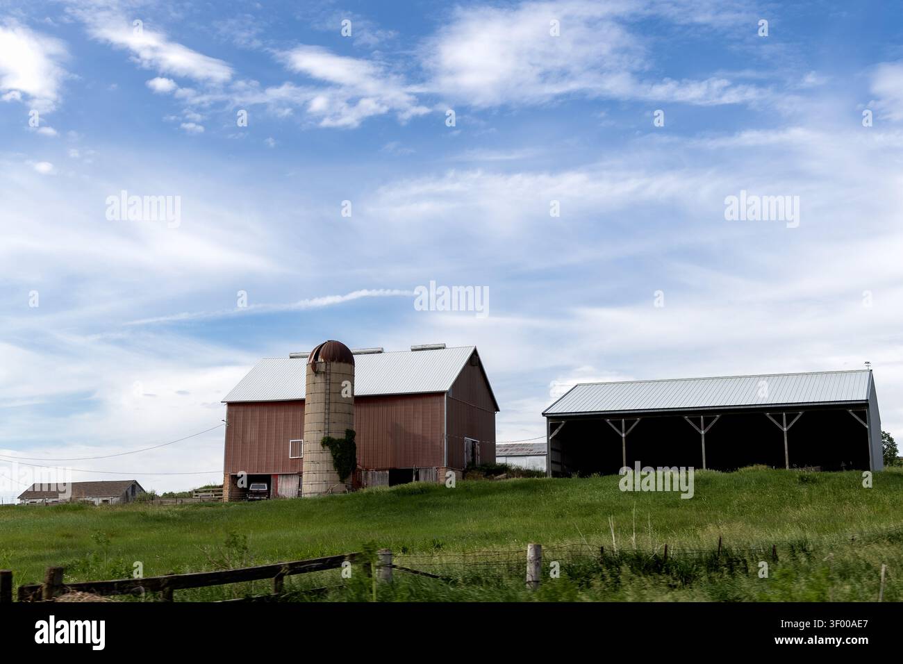 Galena, Illinois, États-Unis - 30 mai 2026 : Grange rouge traditionnelle et silo en béton sur une colline herbeuse sous un ciel d'été dramatique dans la campagne rurale Banque D'Images