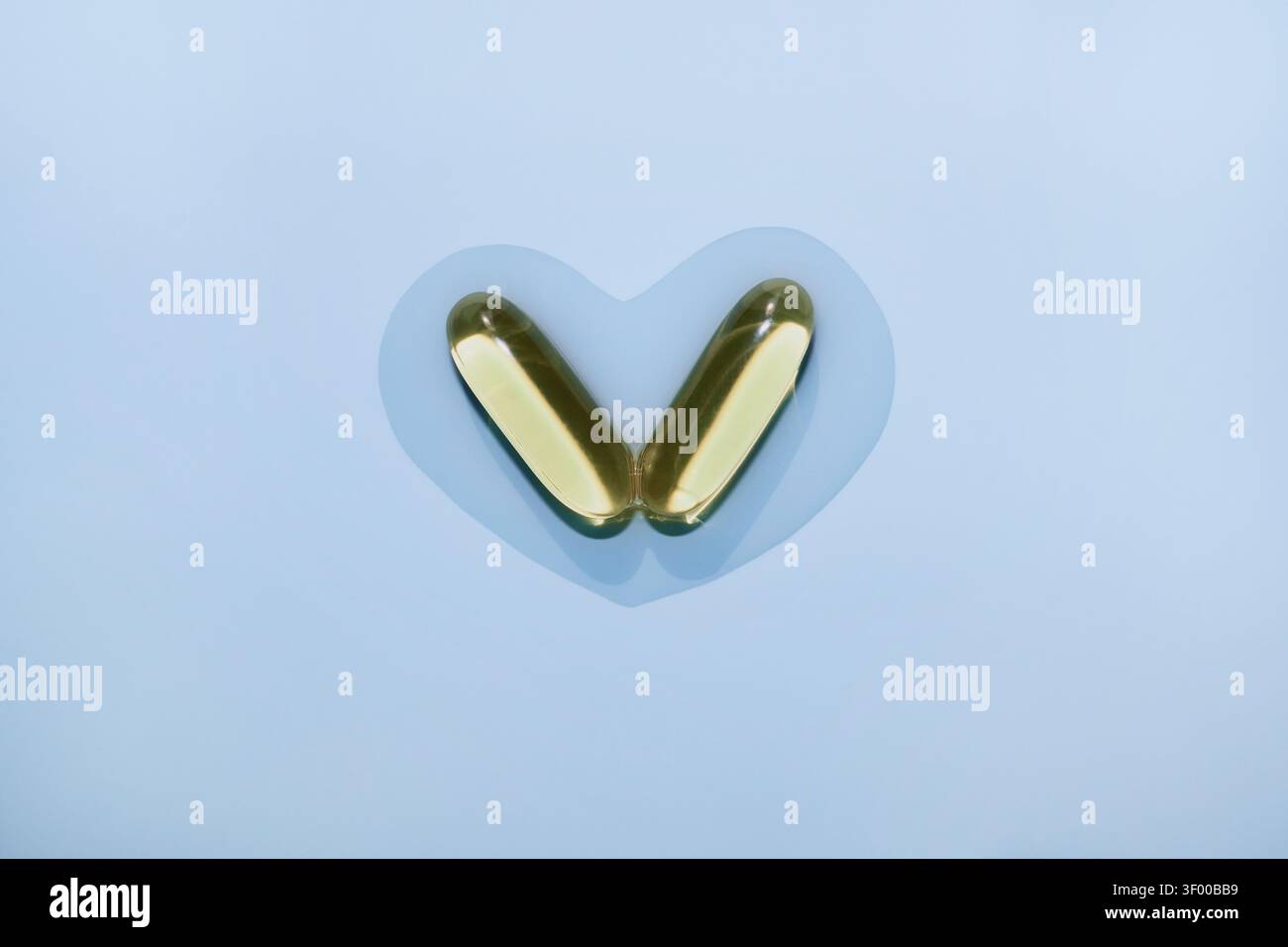 Deux softgels d'huile de poisson créant une forme de coeur sur fond bleu pastel Banque D'Images