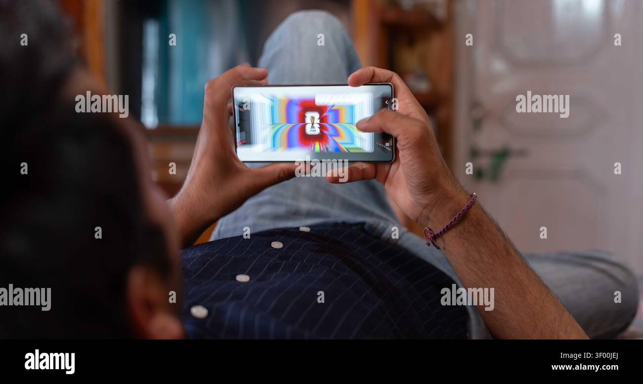 MANDI, HIMACHAL PRADESH, INDE - 5 juillet 2026 : photo fixe au-dessus de l'épaule, à hauteur des yeux, d'un jeune Indien se relaxant à la maison tout en étant couché. Banque D'Images