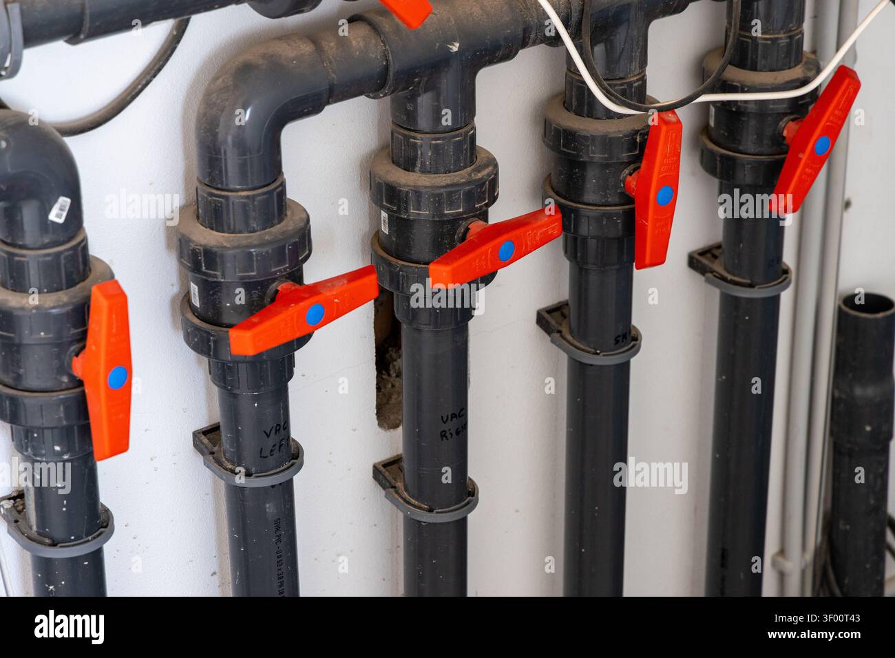 Vue rapprochée d'un réseau complexe de tuyaux gris foncé et de vannes à boisseau sphérique orange vif, suggérant un système d'eau ou de fluide fonctionnel Banque D'Images