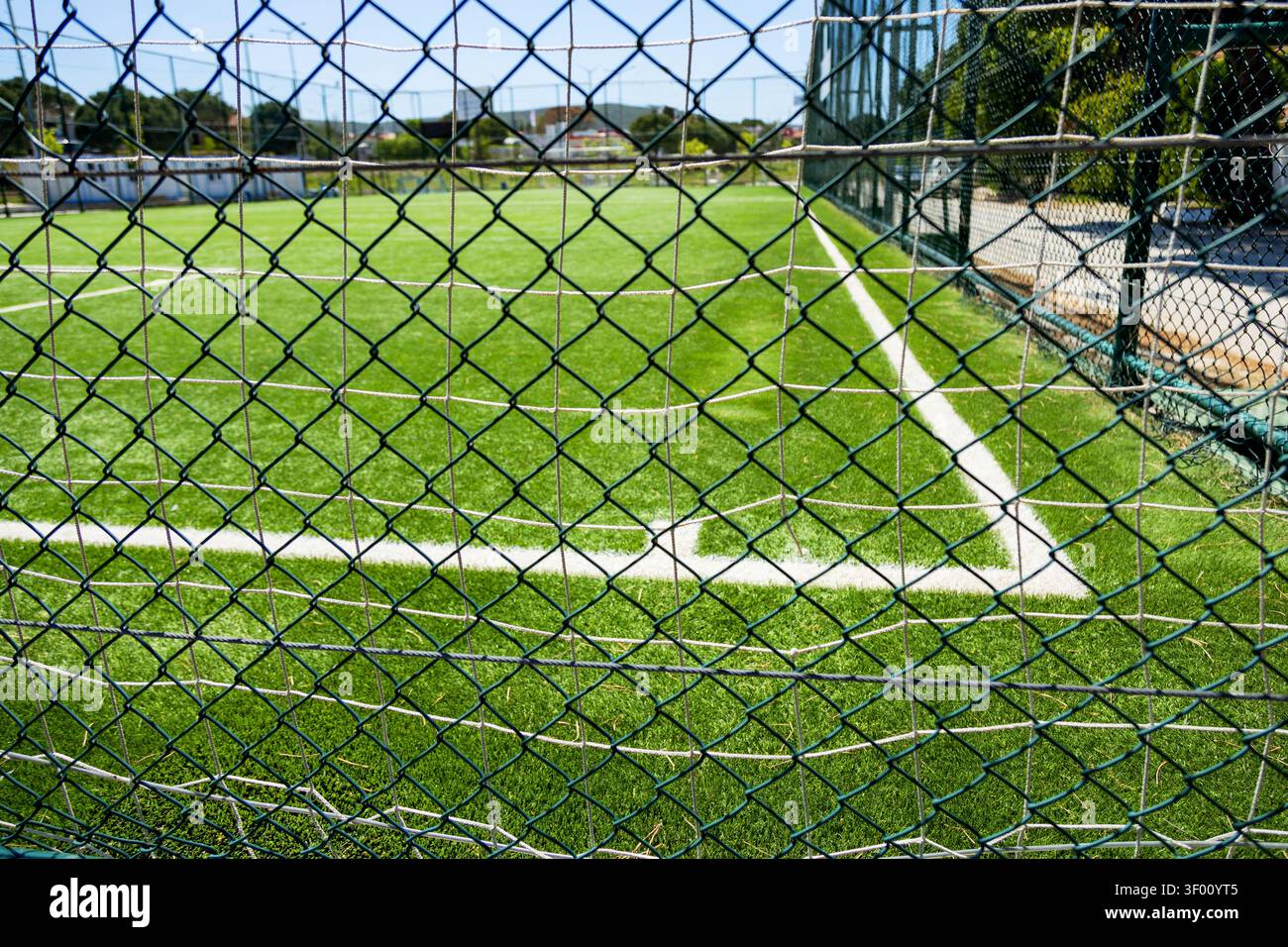 Un terrain de football dynamique est vu à travers une clôture à maillons de chaîne, soulignant l'herbe verte luxuriante et les lignes de démarcation blanches précises, capturant l'essence Banque D'Images