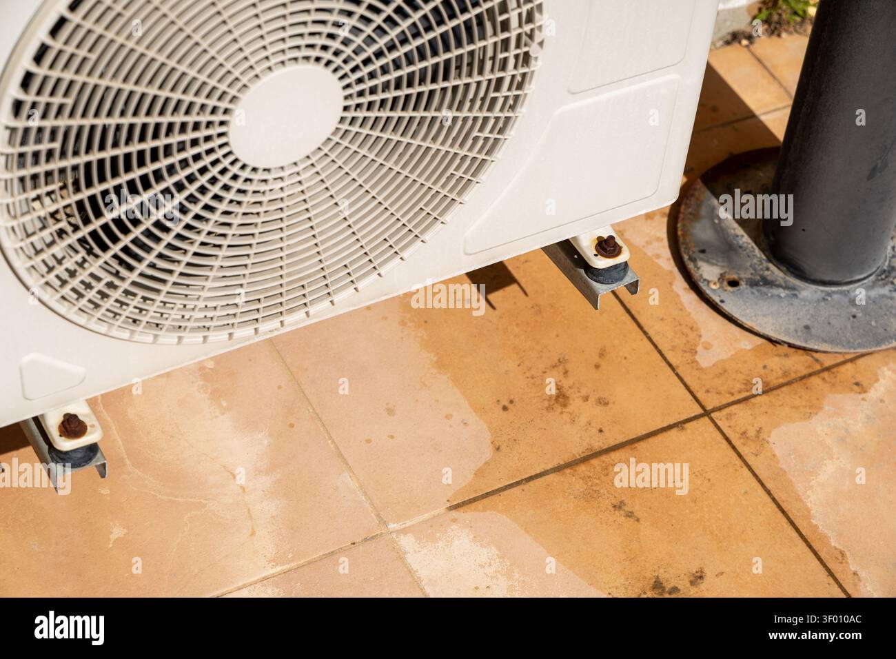 Vue rapprochée du ventilateur et du support de montage d'une unité de climatisation extérieure, montrant des signes d'usure et d'accumulation d'eau sur le patio environnant TI Banque D'Images