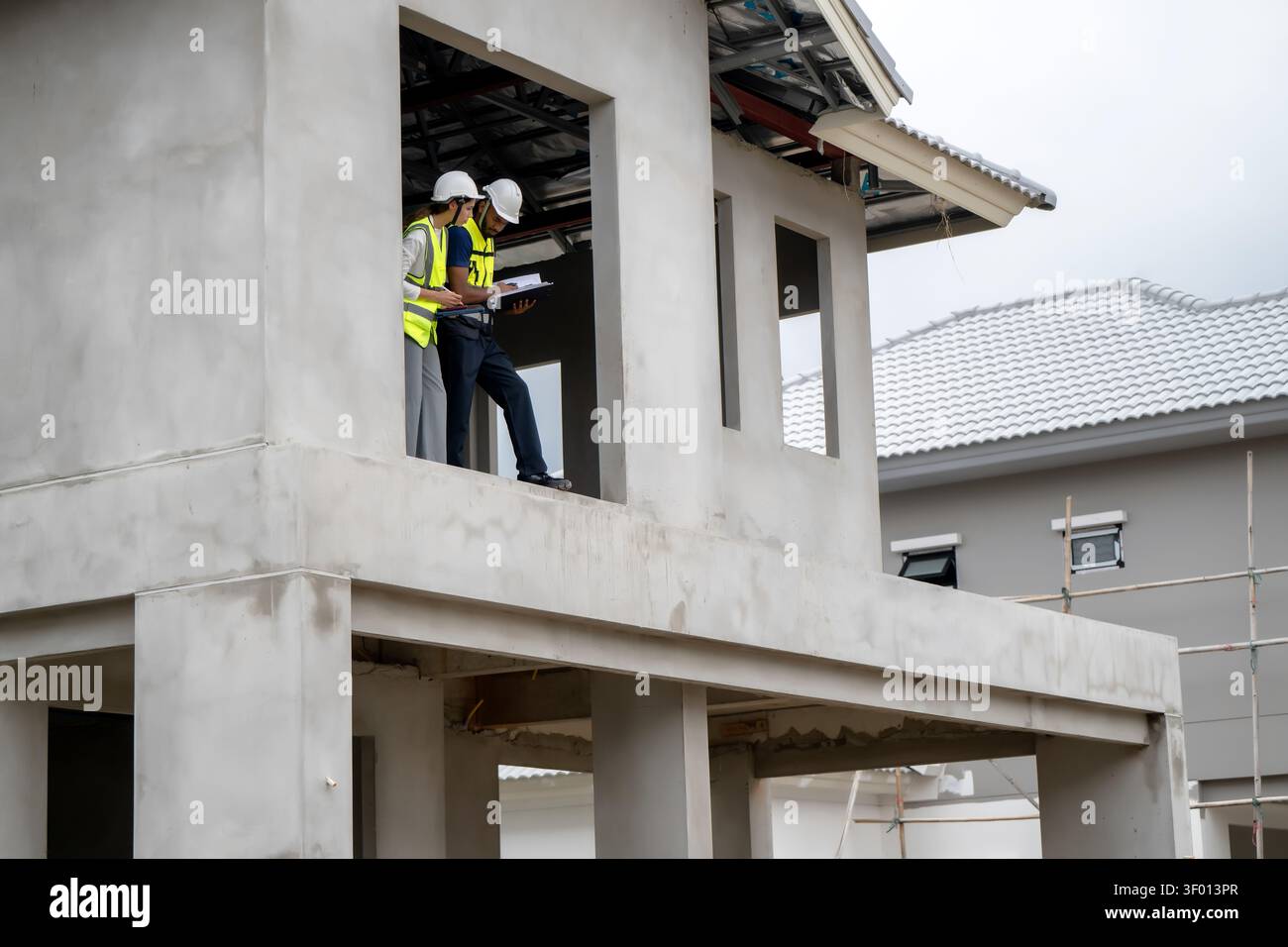 Les gestionnaires de la construction vérifient le presse-papiers sur le balcon du deuxième étage de la maison résidentielle inachevée pendant la journée, concept de gestion de projet et de thé Banque D'Images