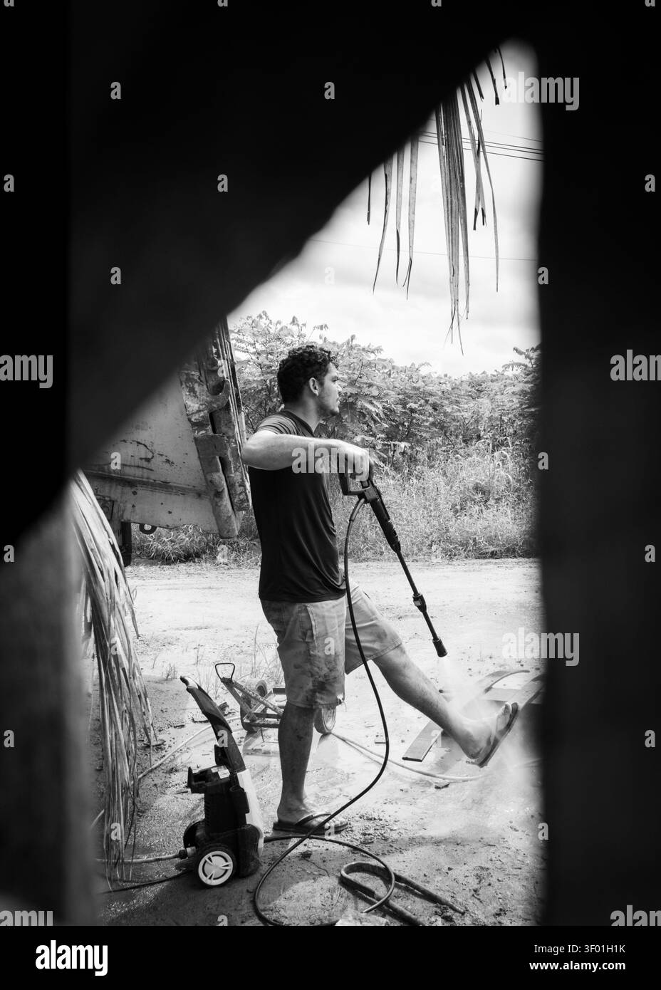 Un homme debout utilisant un nettoyeur haute pression pour se laver les mains, marchant sur un chemin de terre dans une petite ville au Brésil. J'ai vu ce gars travailler et j'ai décidé de sp Banque D'Images