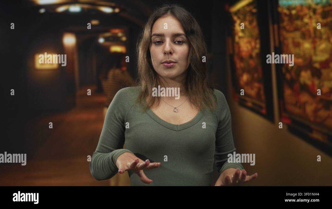 Femme avec les paumes vers le haut et les yeux fermés dans la galerie d'art du bâtiment, portant une chemise verte et un collier de coeur ; réflexion calme. Banque D'Images