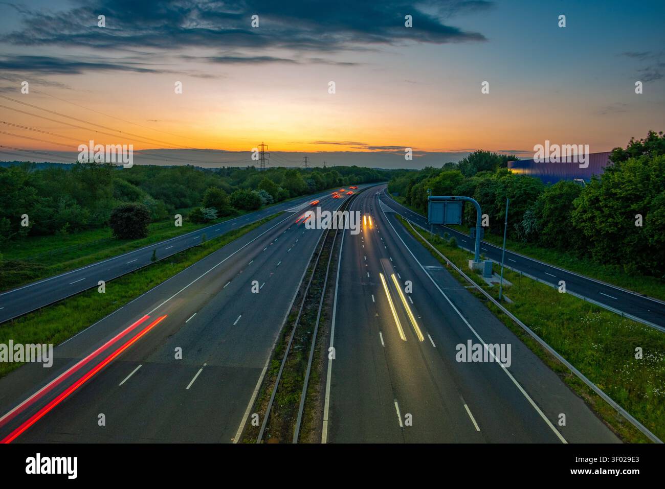 Longue exposition de traînées de lumière de véhicule sur une autoroute M4 à plusieurs voies au coucher du soleil avec un ciel orange horizon et des arbres verts, Royaume-Uni. JCT 13 Banque D'Images