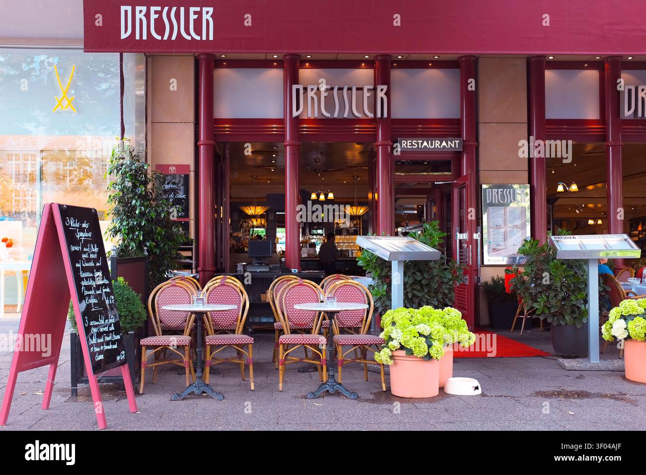 Berlin, Allemagne : le coin salon extérieur élégant de style parisien du restaurant Dressler est agrémenté de chaises en osier rouge, de tables et d'un panneau de menu au tableau noir Banque D'Images