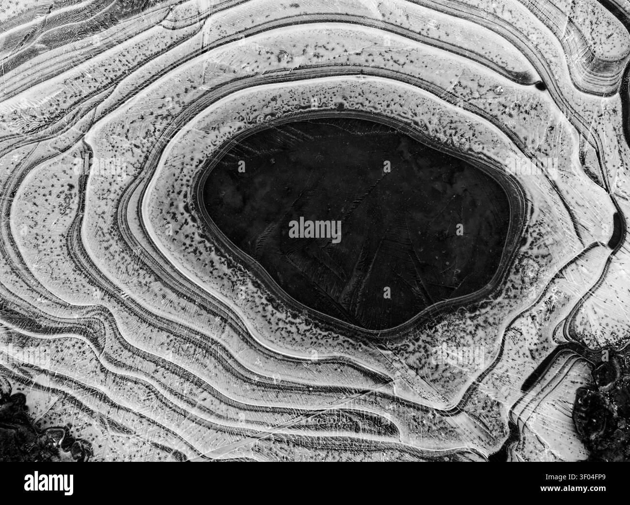 Arrière-plan : ressource graphique d'art naturel. Cercles concentriques de glace sur une flaque gelée en noir et blanc à faible contraste. Banque D'Images