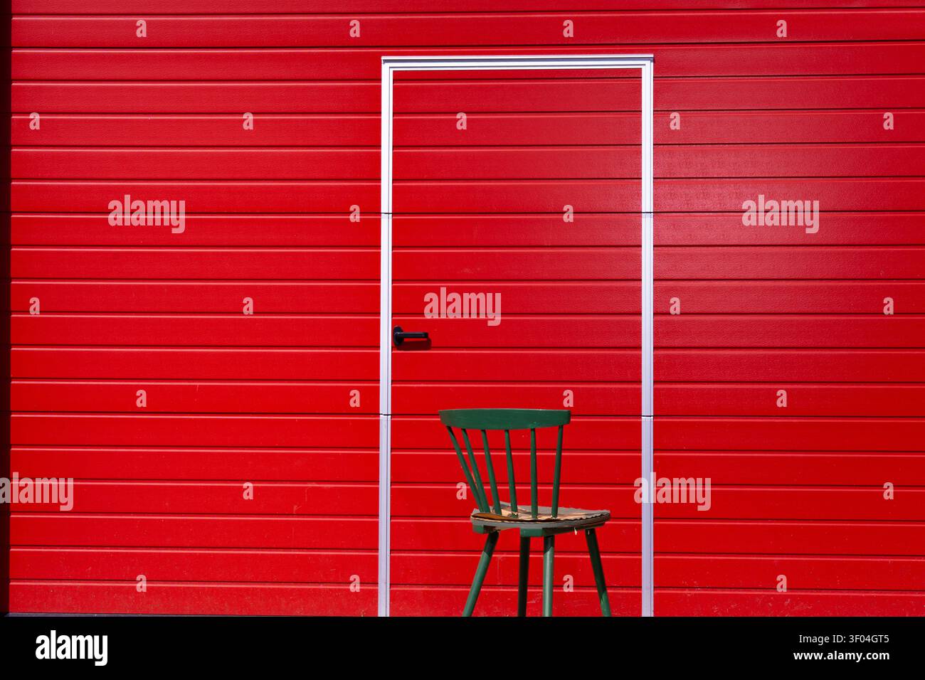 Porte dans un mur rouge avec une chaise verte. Composition contraste de couleurs avec espace de copie. Banque D'Images
